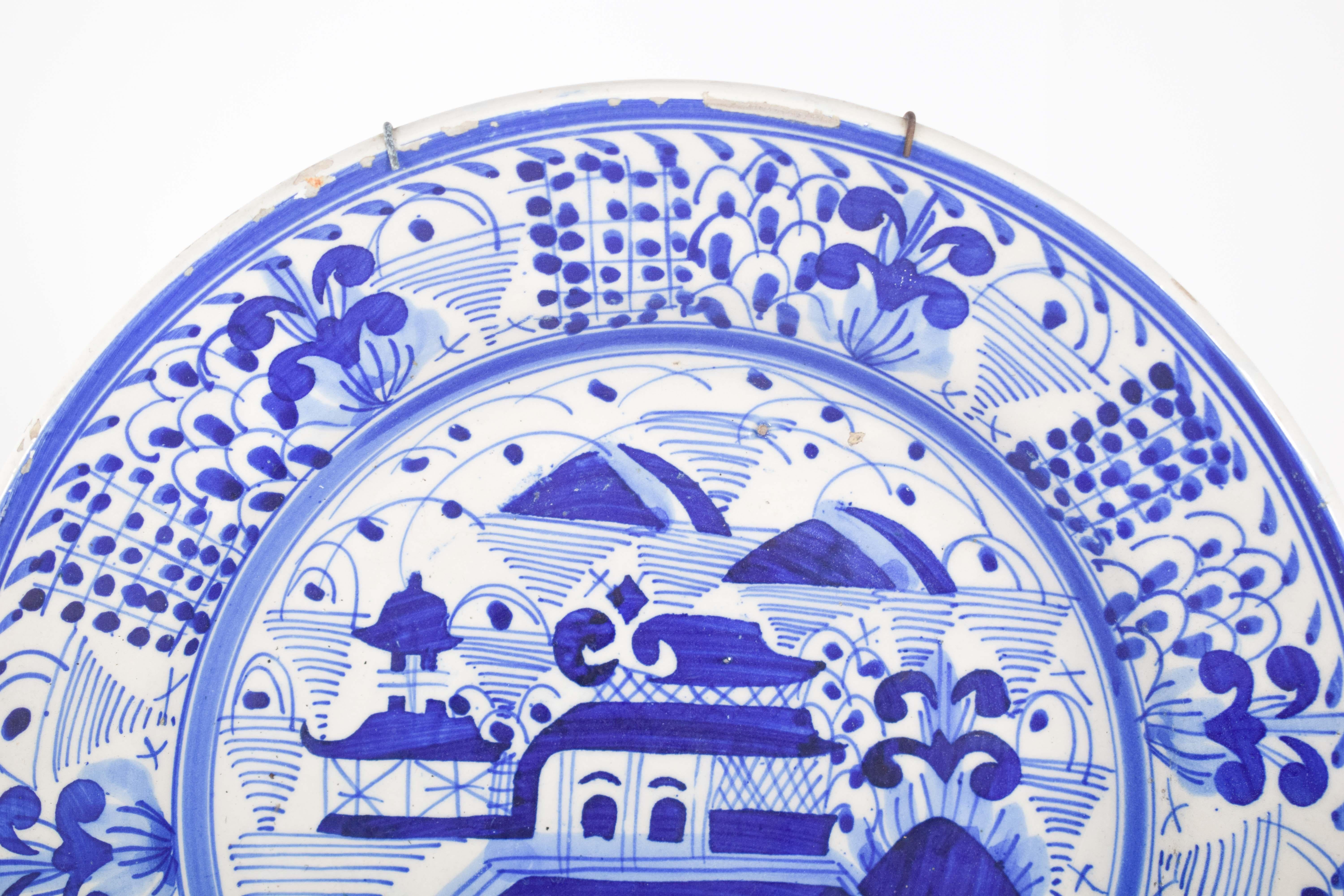 Piatto in terracotta. Decorazioni in bianco e blu con paesaggi fluviali, ponti, case e piante.
Al centro del piatto spicca una scena con pagode e case, circondata da montagne ondulate e vegetazione stilizzata. La rappresentazione centrale, con le