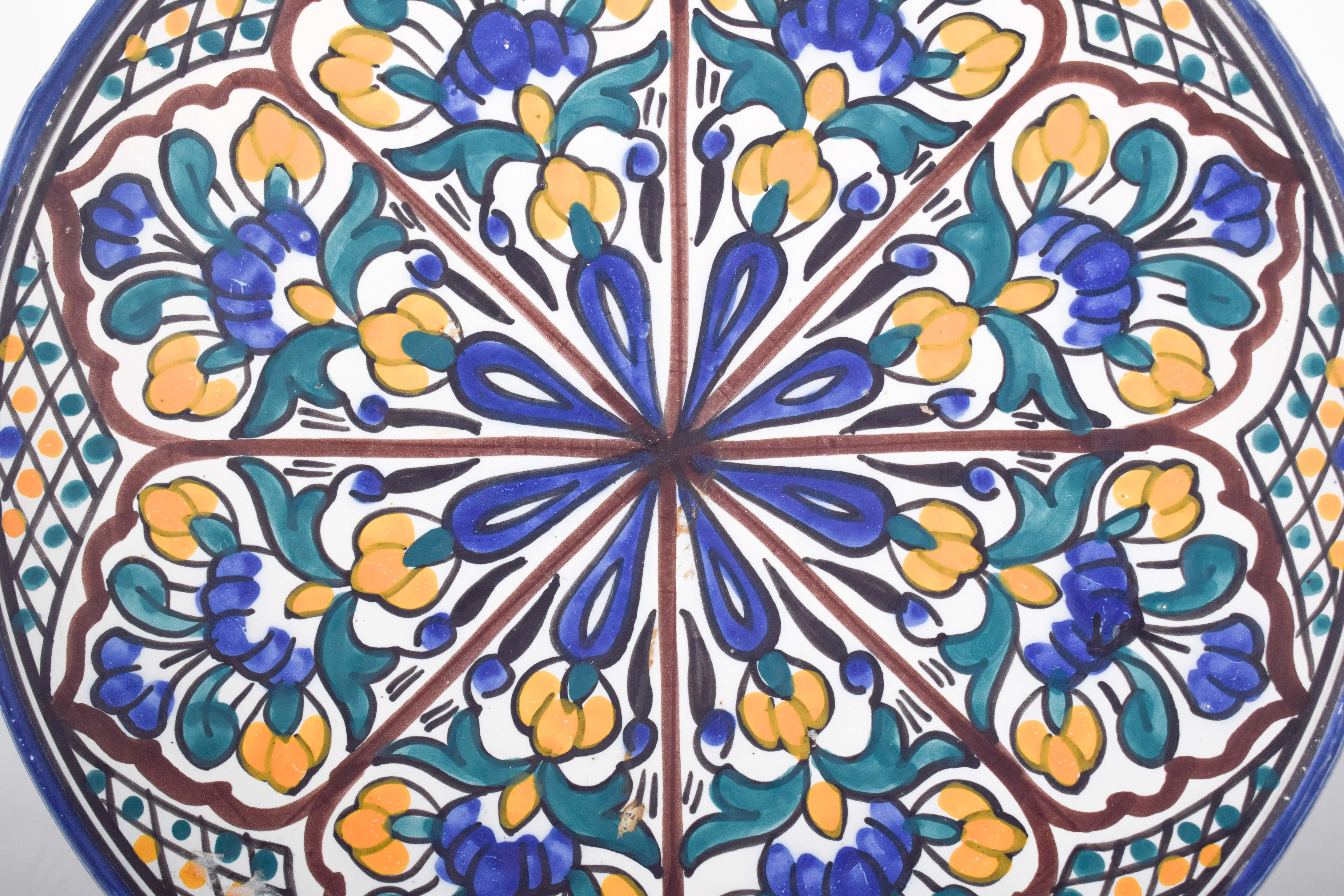 Assiette en faïence portugaise. Décoration polychrome en bleu, vert, jaune et vin, avec des motifs floraux et géométriques, un style souvent associé à l'influence mauresque sur la culture ibérique. La composition symétrique et répétitive des fleurs