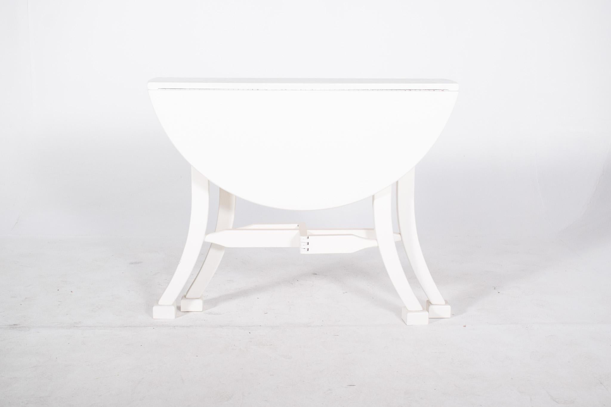Flap table painted white. The two hinged flaps can be lifted to adapt the size of the surface as required, leaving a round table once opened. It rests on four elegant arched legs, ending in square shoes, joined by central ‘X’ crosspieces, which add
