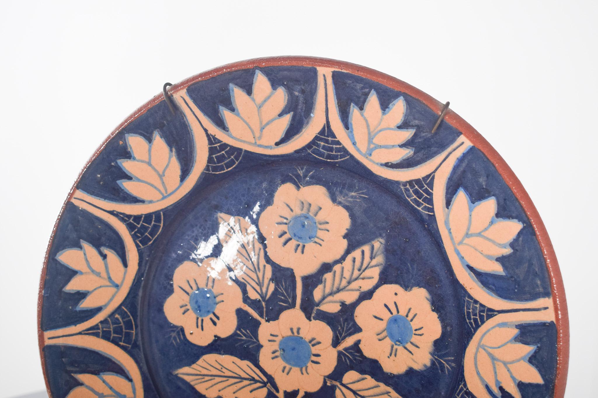 Plat en terre cuite peint à la main.  Décorée de fleurs et de demi-cercles dans les tons bleu et beige. Le dos du plat n'est pas peint, ce qui en fait une pièce rustique faite à la main. 
Le fond est émaillé d'un bleu profond, offrant un beau