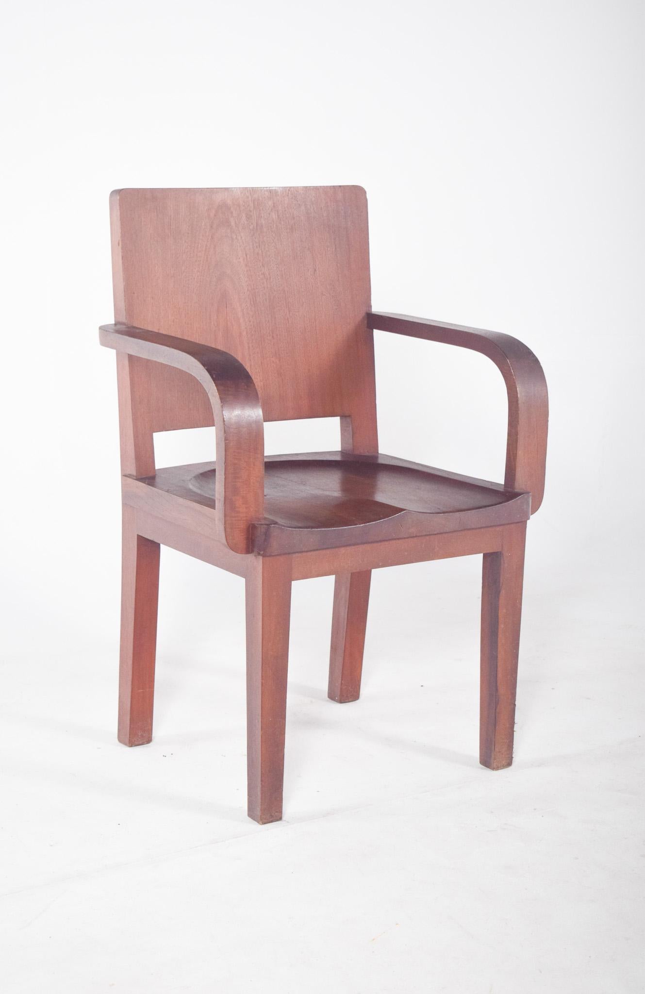 Mahagoni-Sessel. Das robuste Design und die geraden Linien sind typisch für institutionelle Umgebungen oder Büros des 20. Jahrhunderts. Die Rückenlehne und der Sitz sind aus Formholz, mit abgerundeten Ecken und glatter Oberfläche. Die Armlehnen