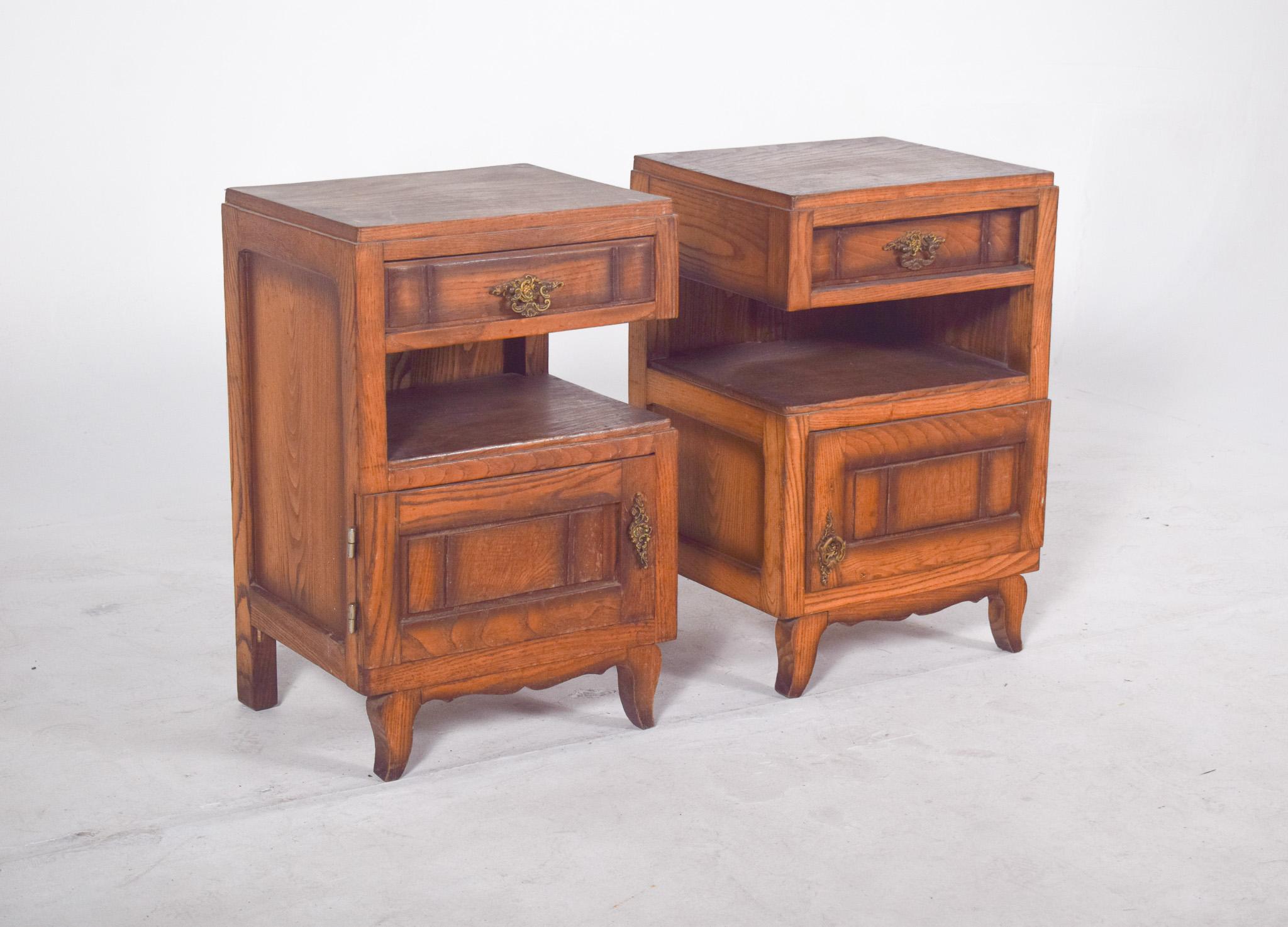 Pair of oak bedside tables. Top drawers with metal handles, a central open niche and a bottom door with a beaded frame and decorative hardware in a classic style. The tables stand on cabriolet legs with a sinuous front cut-out, which add elegance