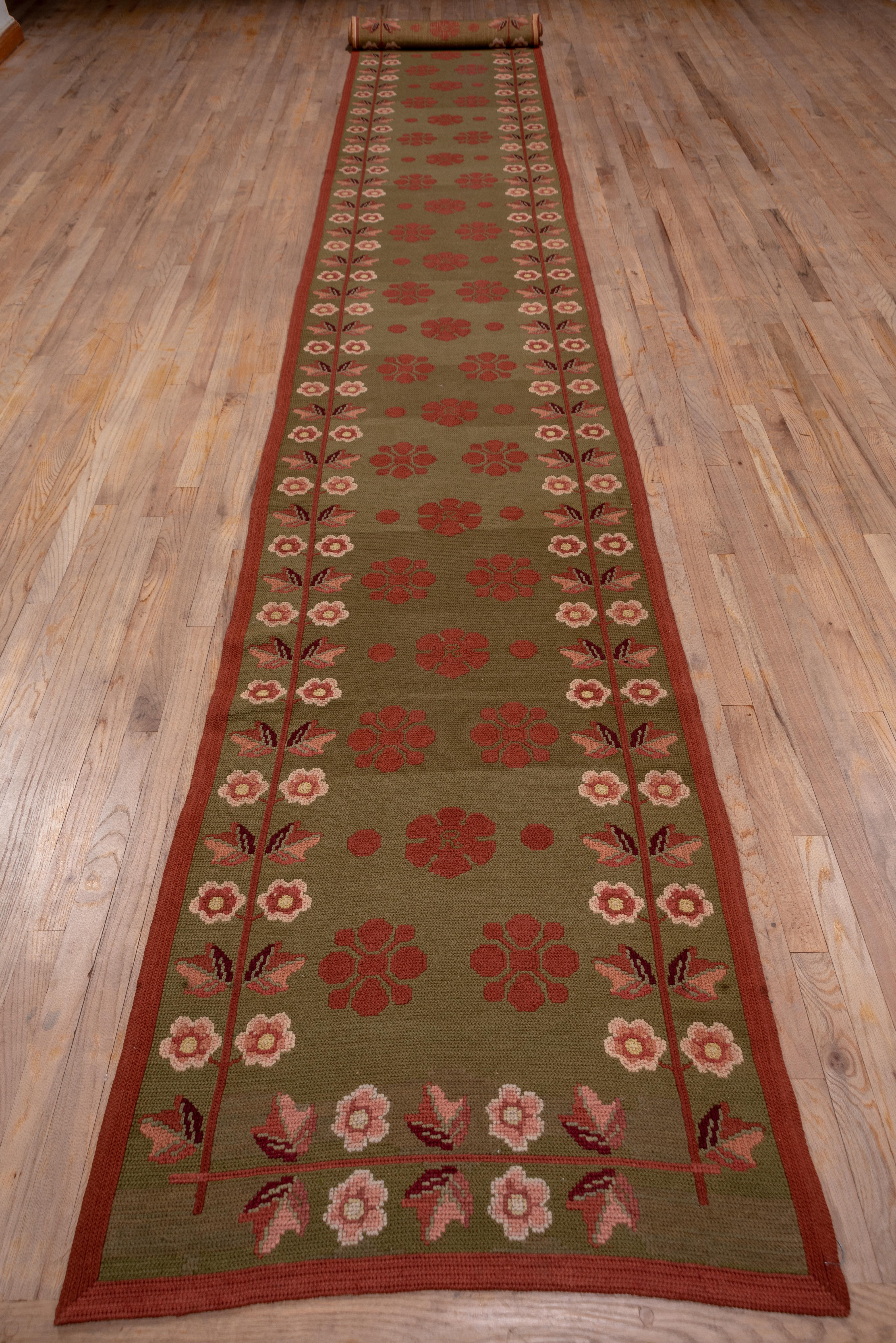 This pileless runner displays red petaled rosettes on a kelly green field with flowering stem border outlines. The surface is executed in a sort of herringbone stitch. The condition is excellent.