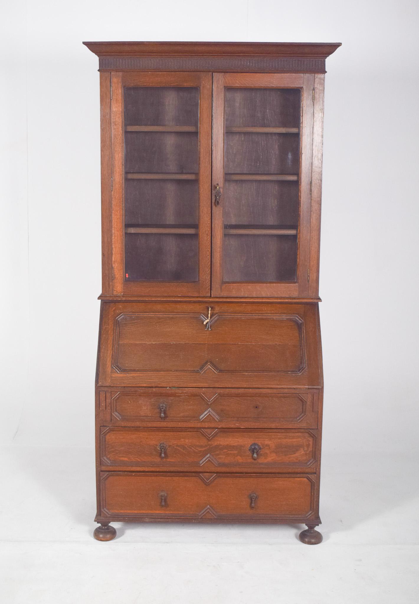 Paper chest of drawers with elevation, in oak. The upper part has a cupboard with two glazed doors and straight mouldings, housing internal shelves for books or other objects, crowned with a pronounced cornice and a frieze carved in a vertical