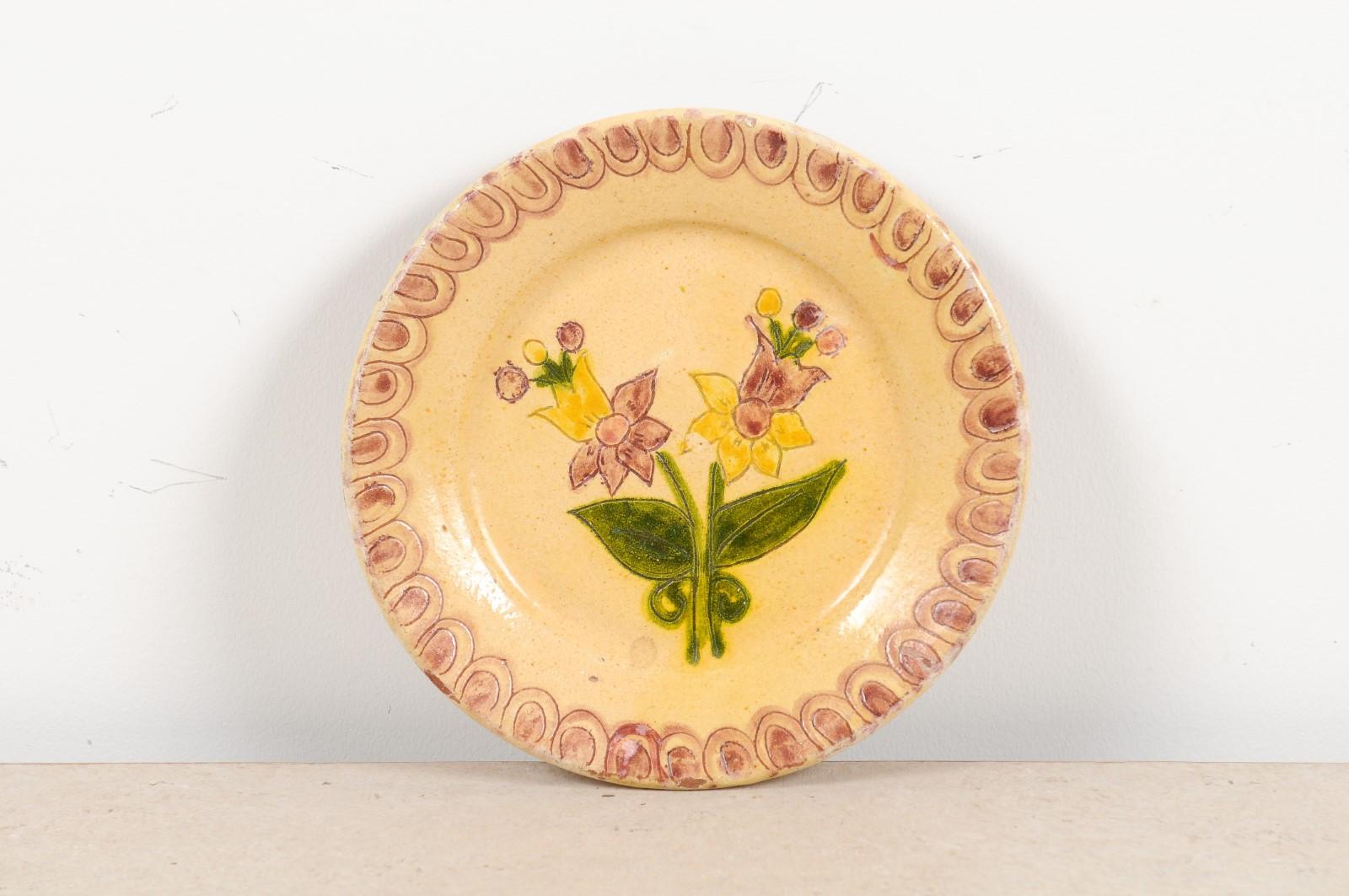 A Portuguese painted clay pottery plate from the early 20th century with floral decor and decorated border. Created in Portugal during the early years of the 20th century, this painted clay plate charms us with its naïve floral decor, showcasing