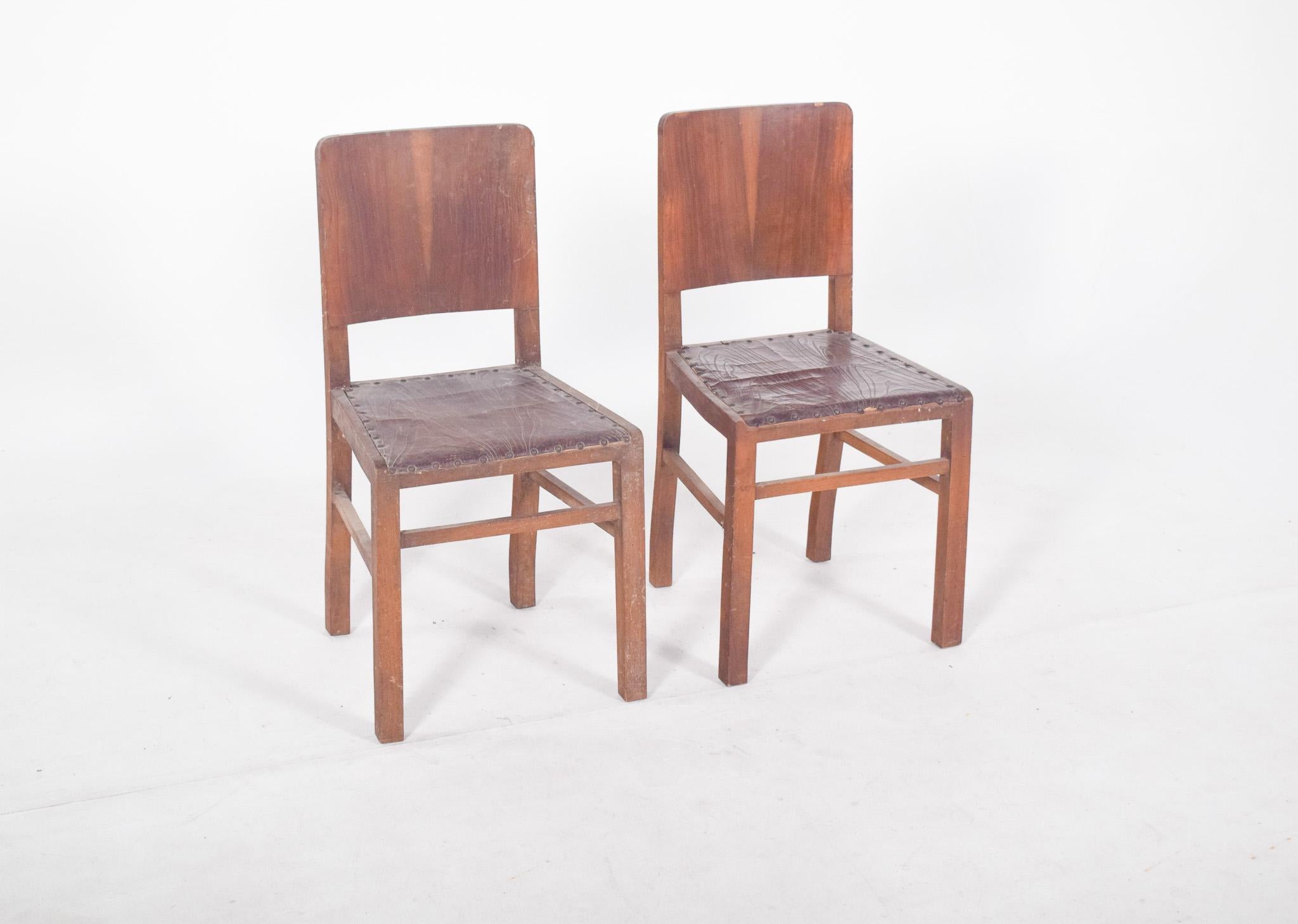 Pair of leather chairs with studs. Straight backrest and upholstered leather seat secured by visible panels that run along the entire upper edge, with a simple and functional structure with straight lines and robust proportions reminiscent of a
