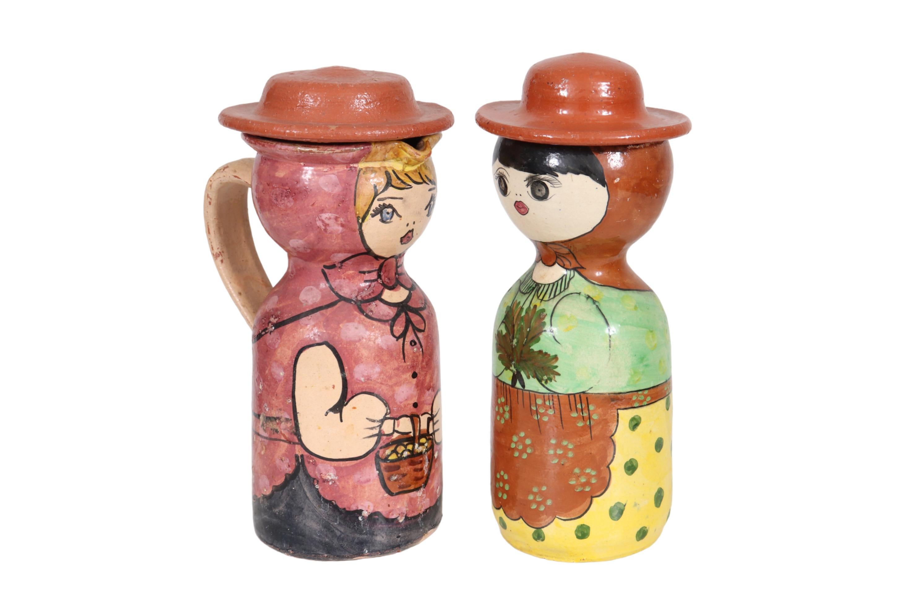 A set of two Portuguese Piracca Redondo pottery lidded jugs, shaped like figures and hand painted to look like women. One has a spout and handle, painted to look like a blonde woman in pink holding a basket. The other is a canister painted to look
