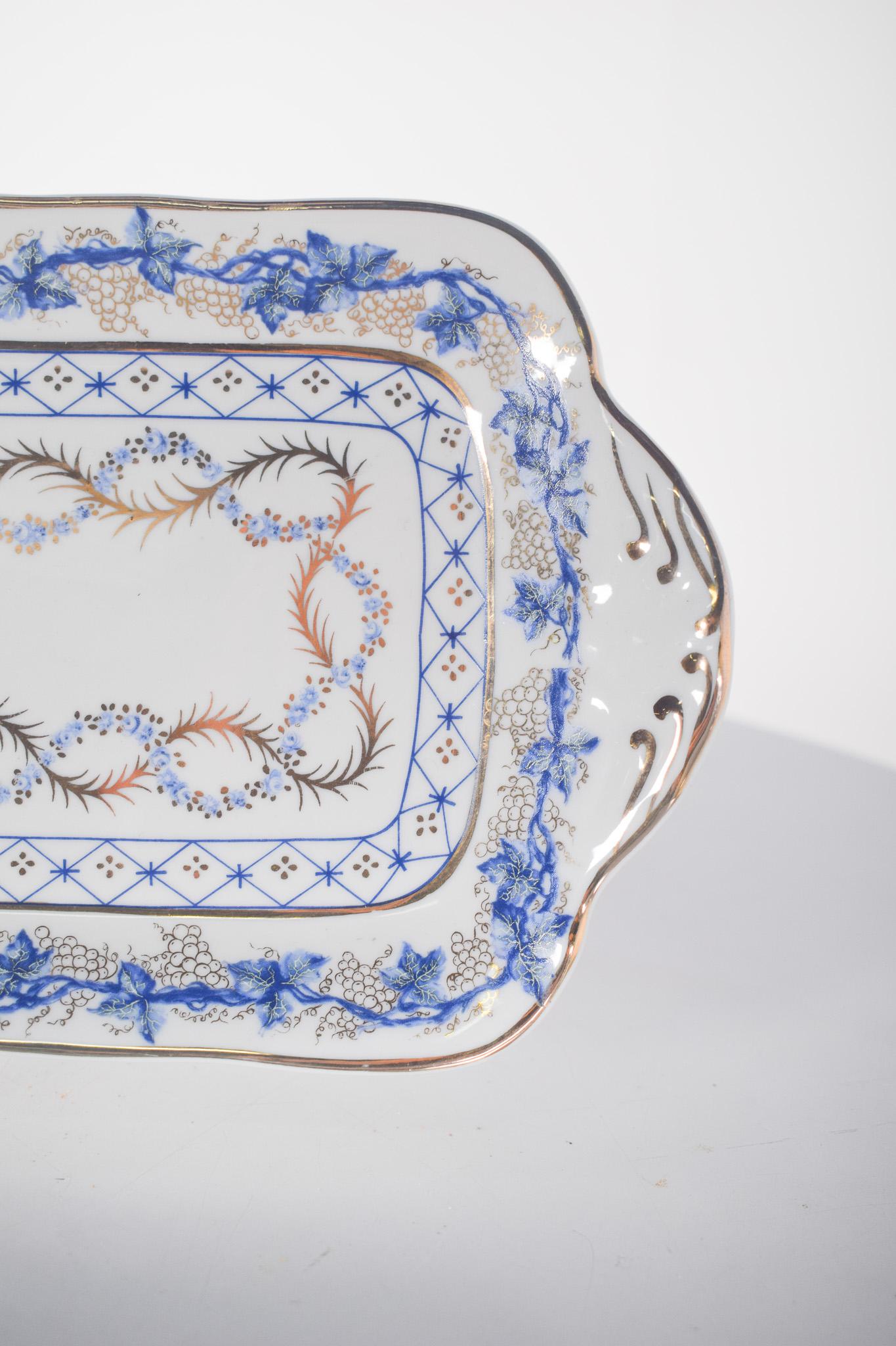 Plat à gâteau en porcelaine portugaise de Vidal Arte. Avec des bords légèrement ondulés et des poignées latérales festonnées, la pièce présente un décor bleu et or raffiné, avec des motifs floraux et géométriques, évoquant le style classique de la