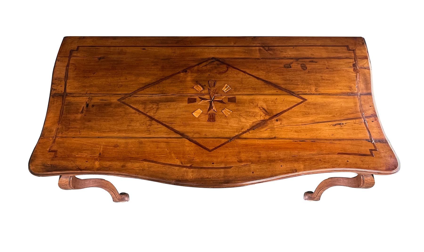 the serpentine top centering an inlaid Maltese Cross, the symbol of protection and a badge of honor, within a diamond and outer inlaid border; over a deeply scalloped apron centering a spherical reserve panel; raised on shapely cabriole supports