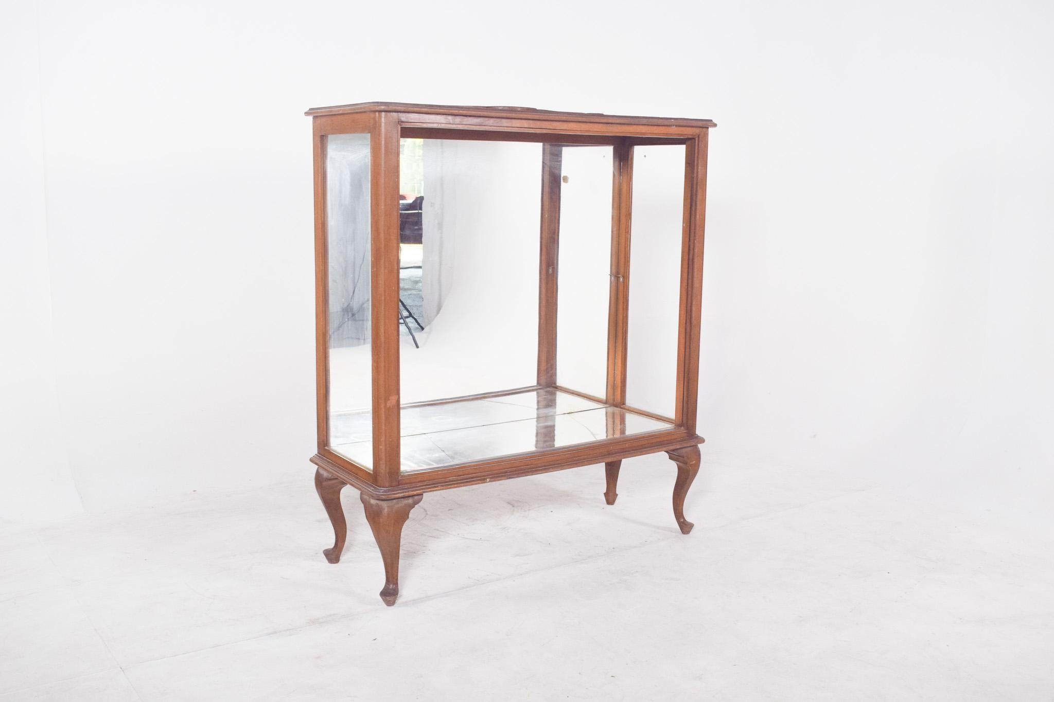 Vitrina de estilo Queen Anne. La estructura de madera y todos los laterales de cristal proporcionan una amplia visibilidad interior y resaltan con elegancia los objetos expuestos. La parte trasera espejada contribuye a la sensación de profundidad y