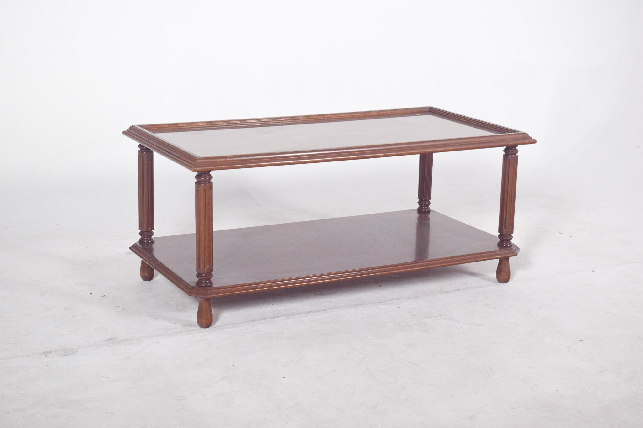 Rectangular coffee table with glass top. The design is classic, with four elegant turned and grooved vertical legs that give the piece its lightness. The base is reinforced by a lower wooden shelf, useful for both storage and decorative support,