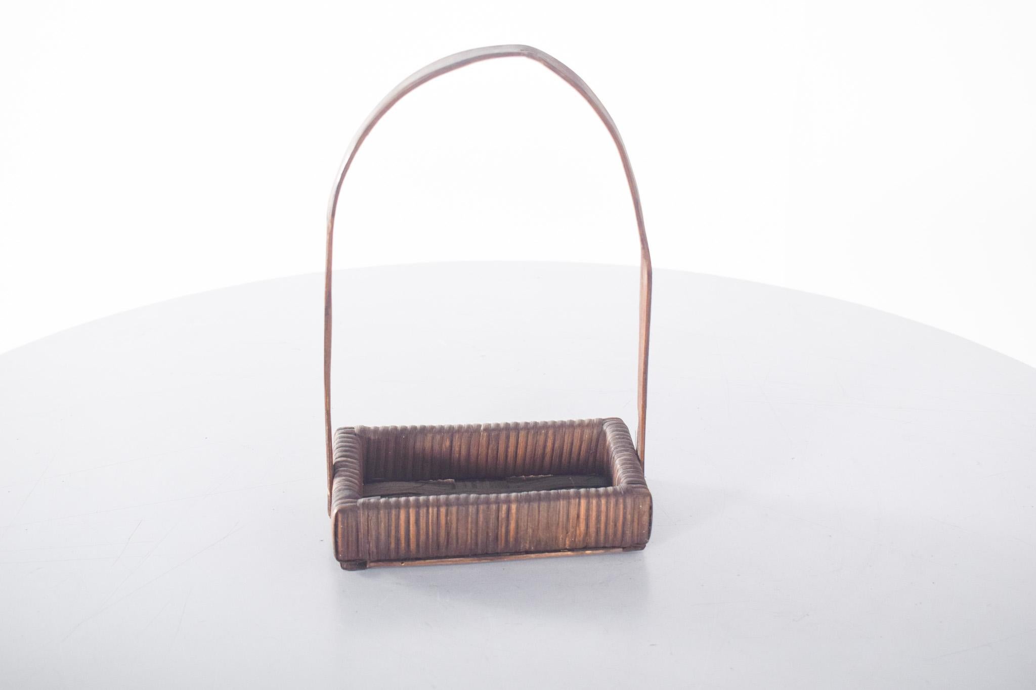 Rectangular wicker basket. It has a firm base in interwoven straw with a reinforced structure at the edges, revealing careful craftsmanship. The high, wide, one-piece handle is inserted at the ends of the base, providing stability and functionality