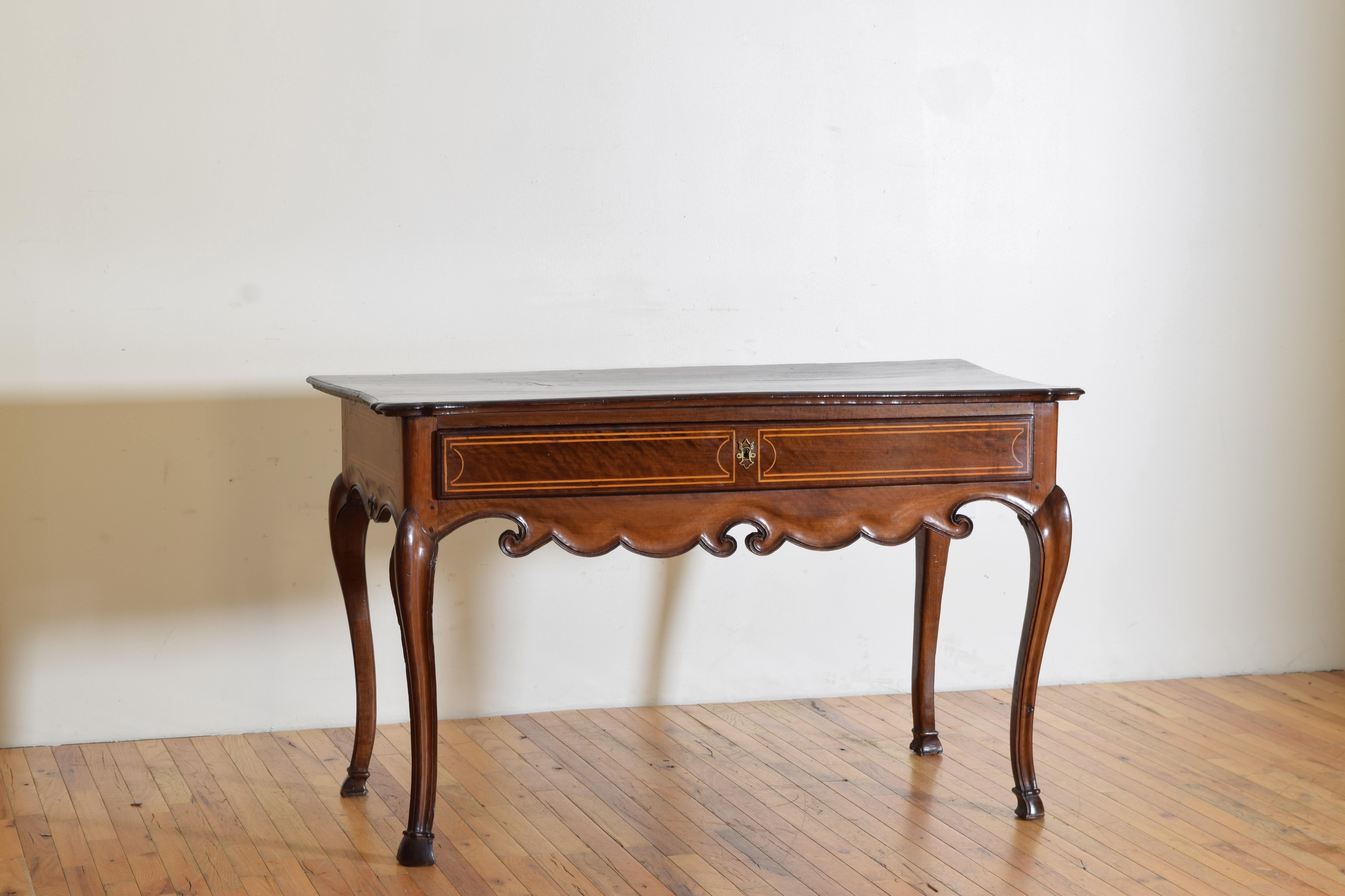 Unique in design and constructed entirely of dark walnut with traces of ebonization at hight points and having a slightly serpentine shaped top with flared sides atop a case housing one drawer with inlaid banding, the apron masterfully carved,