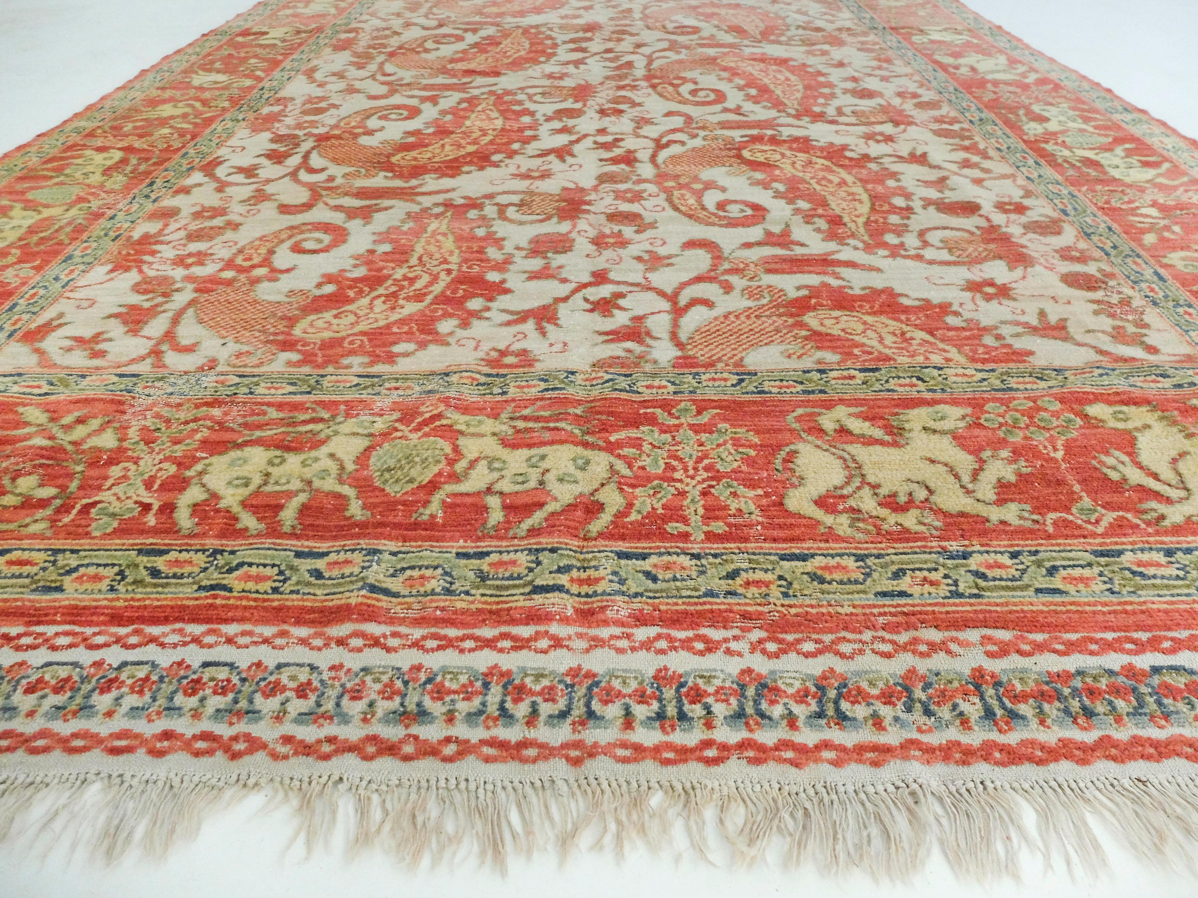 This stunning antique Portuguese runner displays the most exquisite of warm tones. It has soft red-orange colors intermixed with gold tones. The center is patterned with paisley-like shapes while the border is decorated with animals including deer