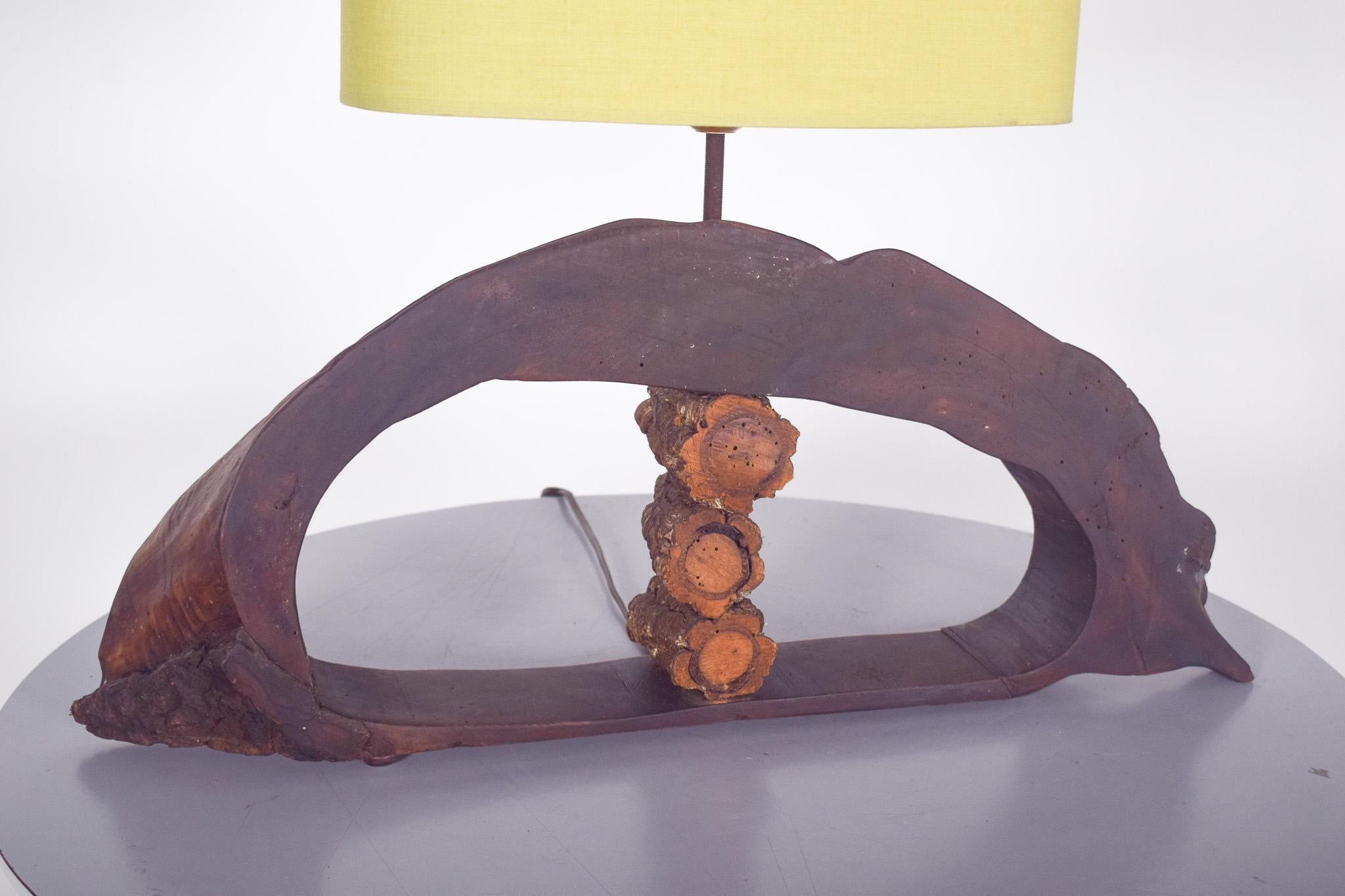 Rustic handmade lamp. Made with a natural wood base and a yellow fabric lampshade. The base structure maintains the organic shape of the wood, creating a unique and naturalistic design. The wood has a dark tone and a rustic finish, with visible