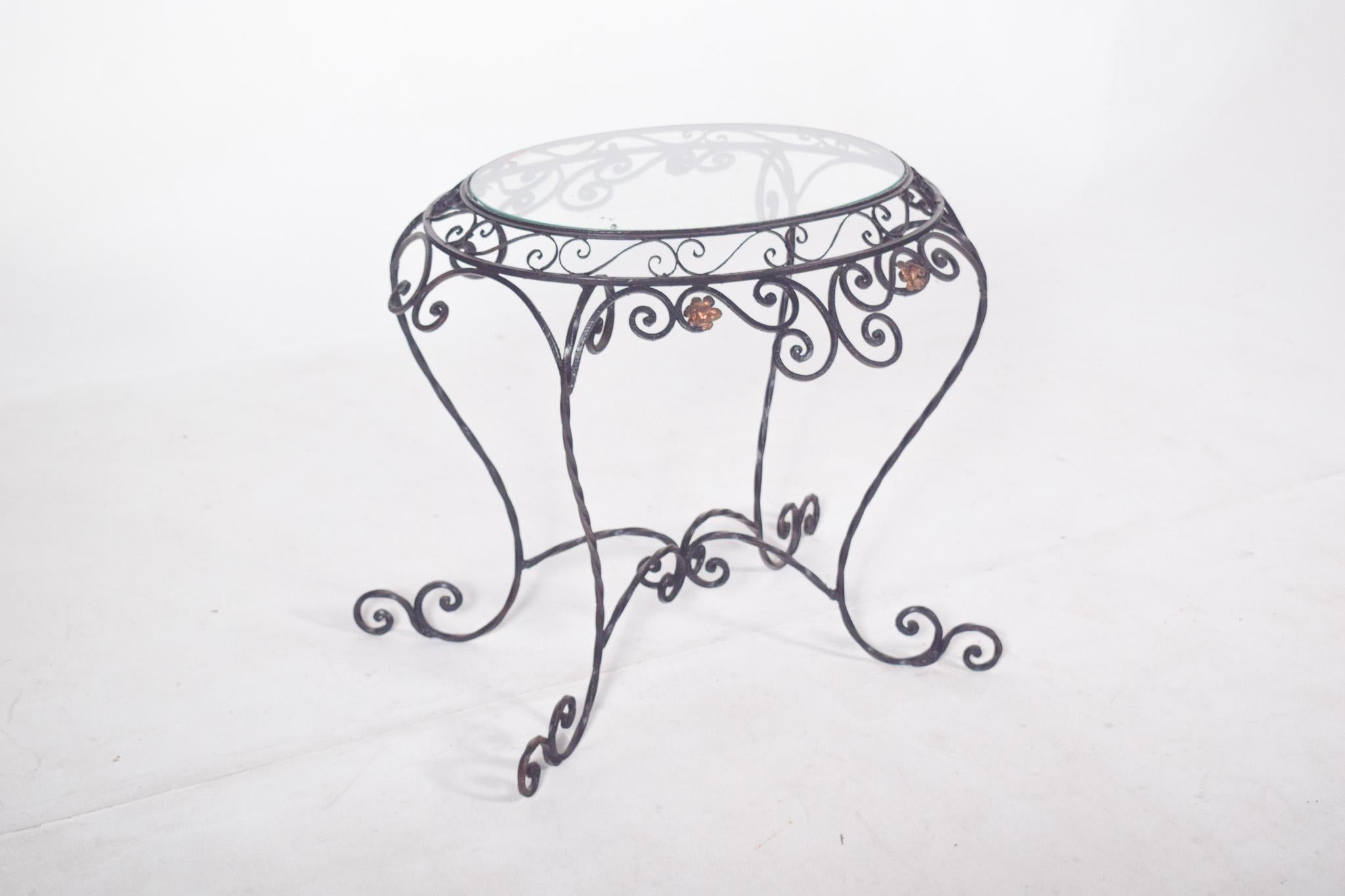 Oval table in wrought iron. The structure features delicate curvilinear arabesques all over the base, with the volute legs and the floral elements applied in gold metal highlighting the set with small touches of colour. The sinuous lines give the