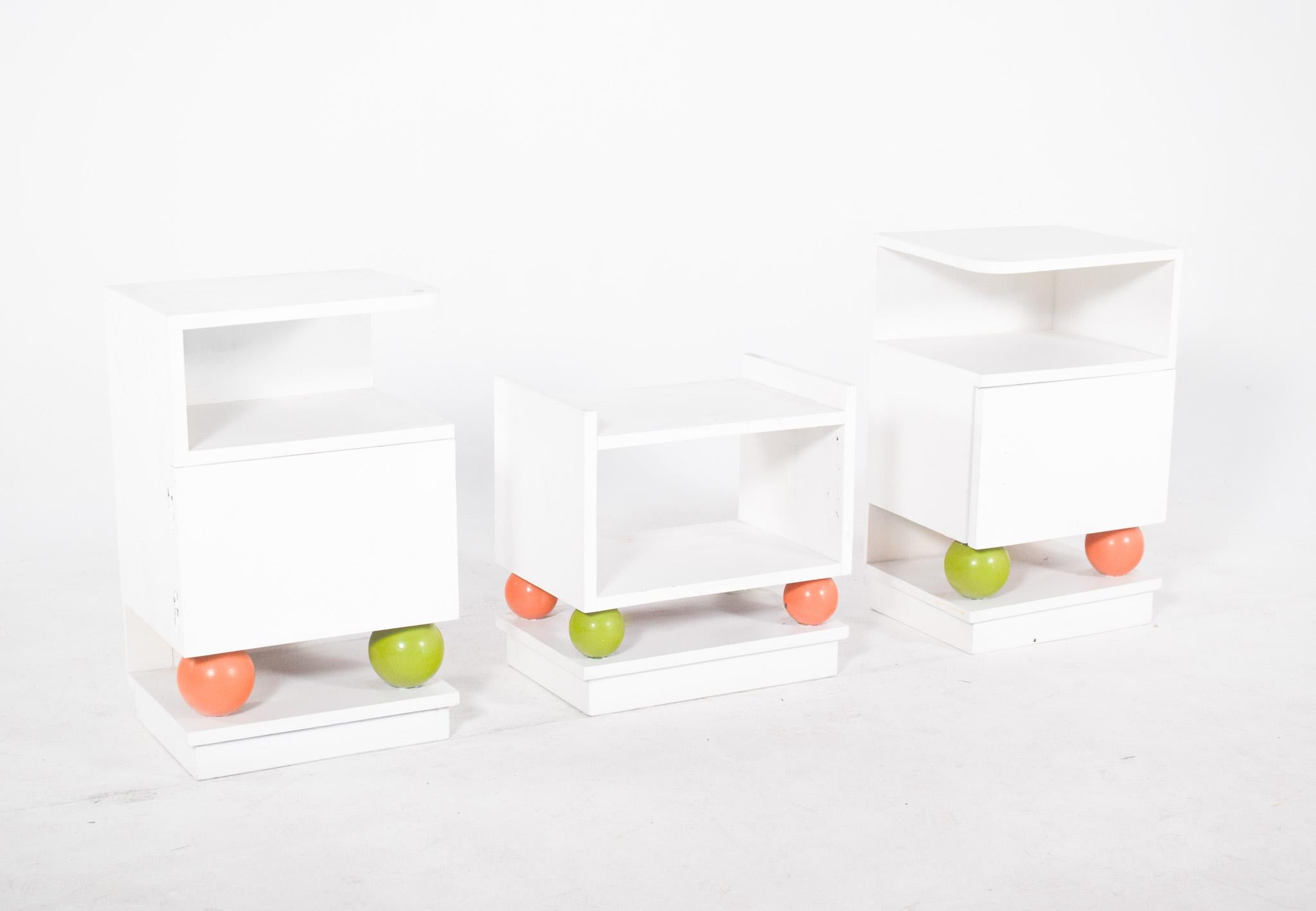 Set of two bedside tables and a bench. In white painted wood, their striking feature is the base resting on coloured balls, green and orange, which give them an original and relaxed look. The bedside tables have an open top niche and a bottom