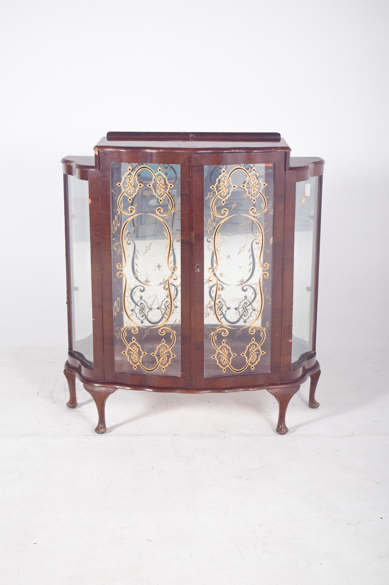 Vitrine de magasin avec verre peint en or. D'inspiration Art déco, avec une structure en bois et une façade incurvée, elle comporte deux portes vitrées au centre, flanquées de fenêtres latérales incurvées, qui confèrent à la pièce légèreté et