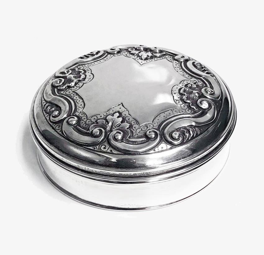 Portuguese 833/1000 silver box with gilded interior. The cover with engraved pin pricked and embossed scroll foliate decoration, vacant centre. The box plain, with moulded upper and lower rims. Gondomar, 1938. Measures: Diameter 4.63 inches., height