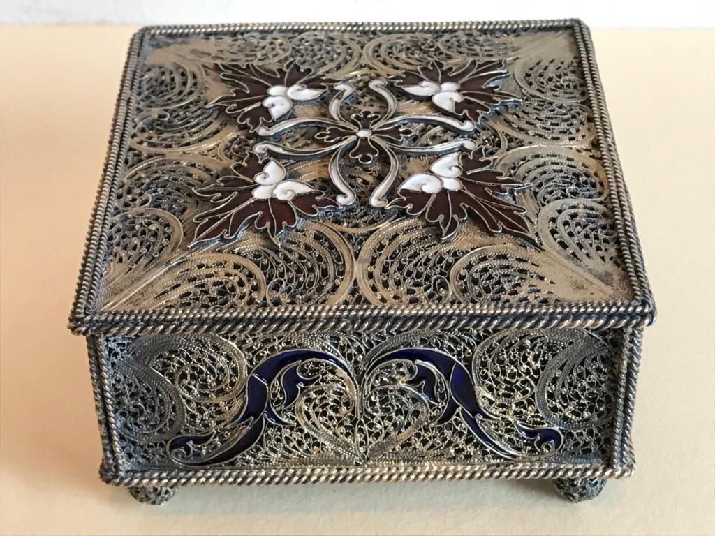 A silver trinket box with exquisite filigree work throughout, including the bottom and the feet. With white and red enamel decoration on the top and deep blue on the side. The delicate workmanship is true art. Oporto, Portugal hallmarks on the rim
