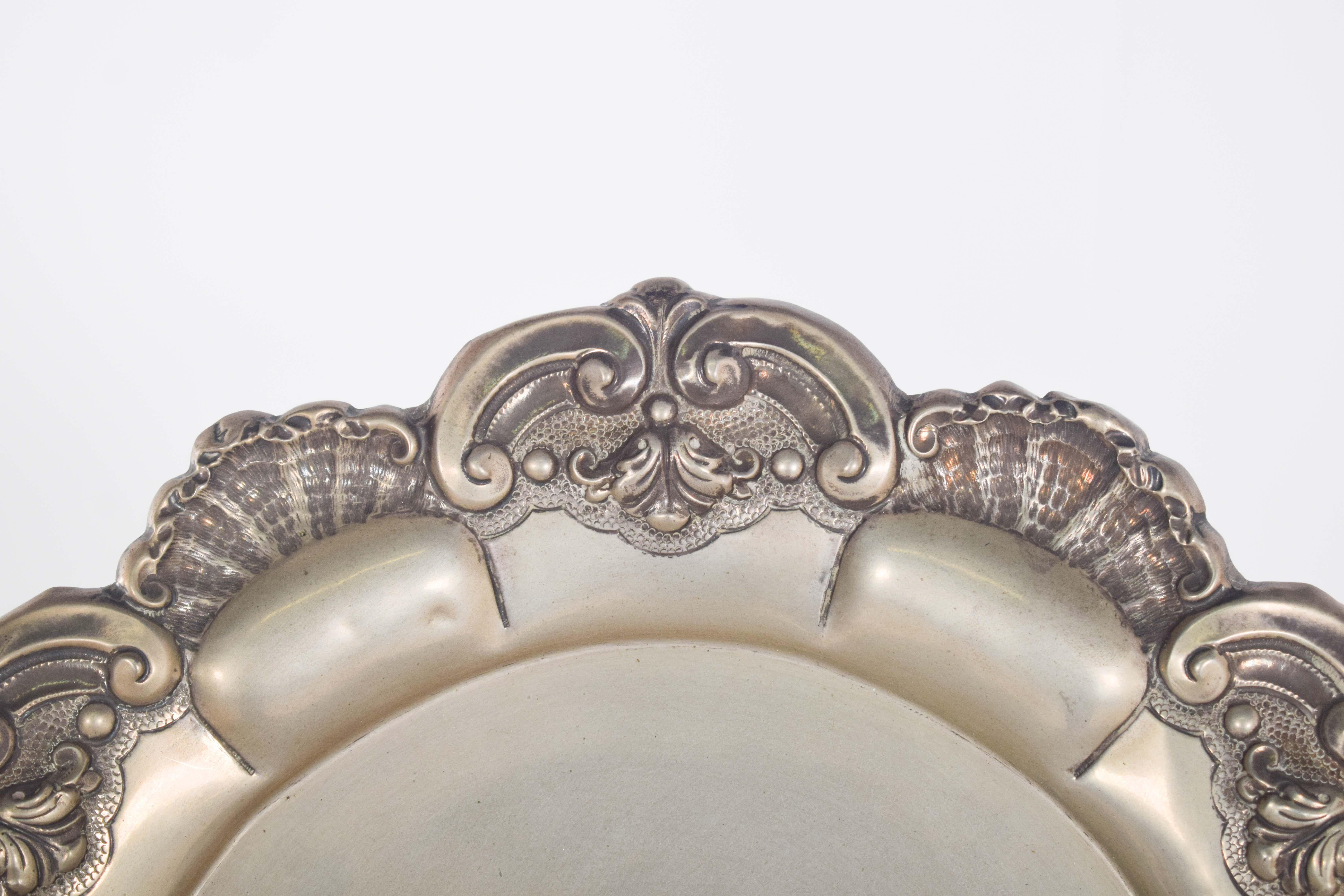Vassoio d'argento portoghese. Decorazione a rilievo e traforata, con fogliame a volute e conchiglie. Le conchiglie si combinano con le curve sinuose e i piccoli dettagli floreali, creando una cornice dinamica ed elegante sul bordo.
La ricchezza dei