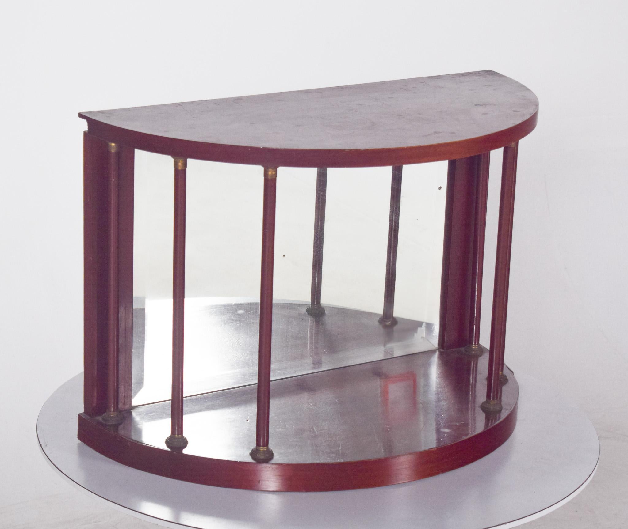 Piccolo espositore da parete a mezzaluna. In legno verniciato con uno specchio sullo sfondo, disegnato a forma di mezzaluna e sostenuto da eleganti colonne verticali che alternano elementi in legno e metallo, probabilmente ottone. Il suo design