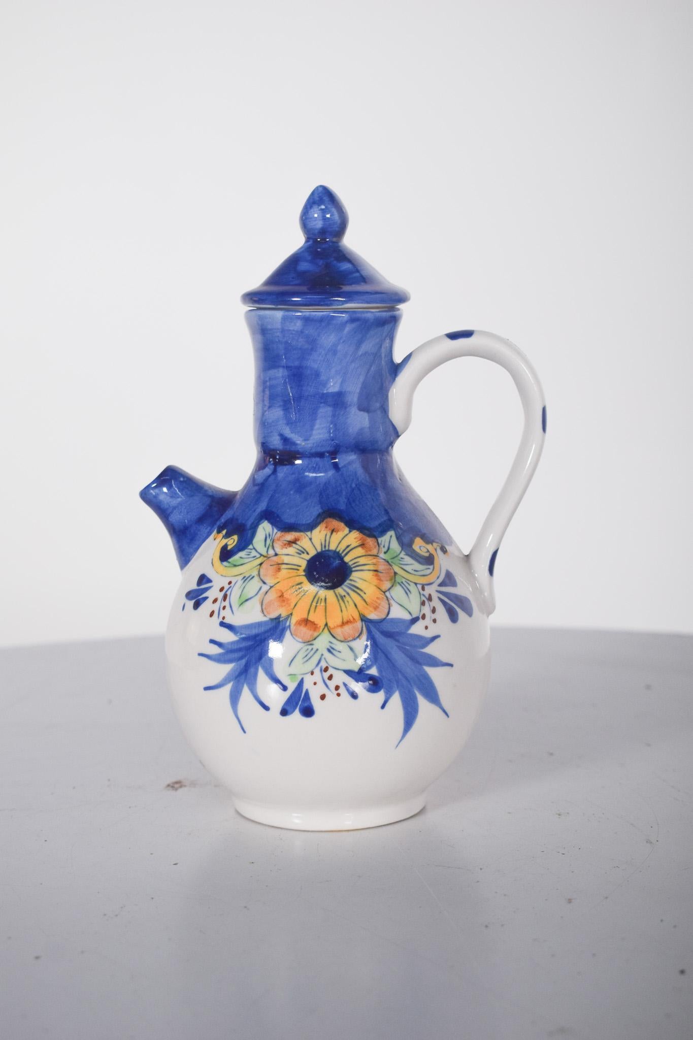Piccolo vaso di ceramica con coperchio. Con un'armoniosa forma arrotondata e rigonfia, ha un beccuccio rotondo corto e leggermente angolato, un manico delicatamente curvo e un coperchio appuntito che si adatta perfettamente alla parte superiore.
La