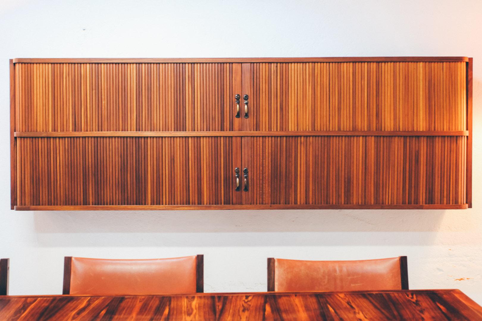 Teak wall mounted tambour door shelf. There are two compartments on the cabinet with sliding doors, metal handles and door lock. One of the shelf is a file and the other one is opened. This piece was manufactured in Portugal during the 50s. Is