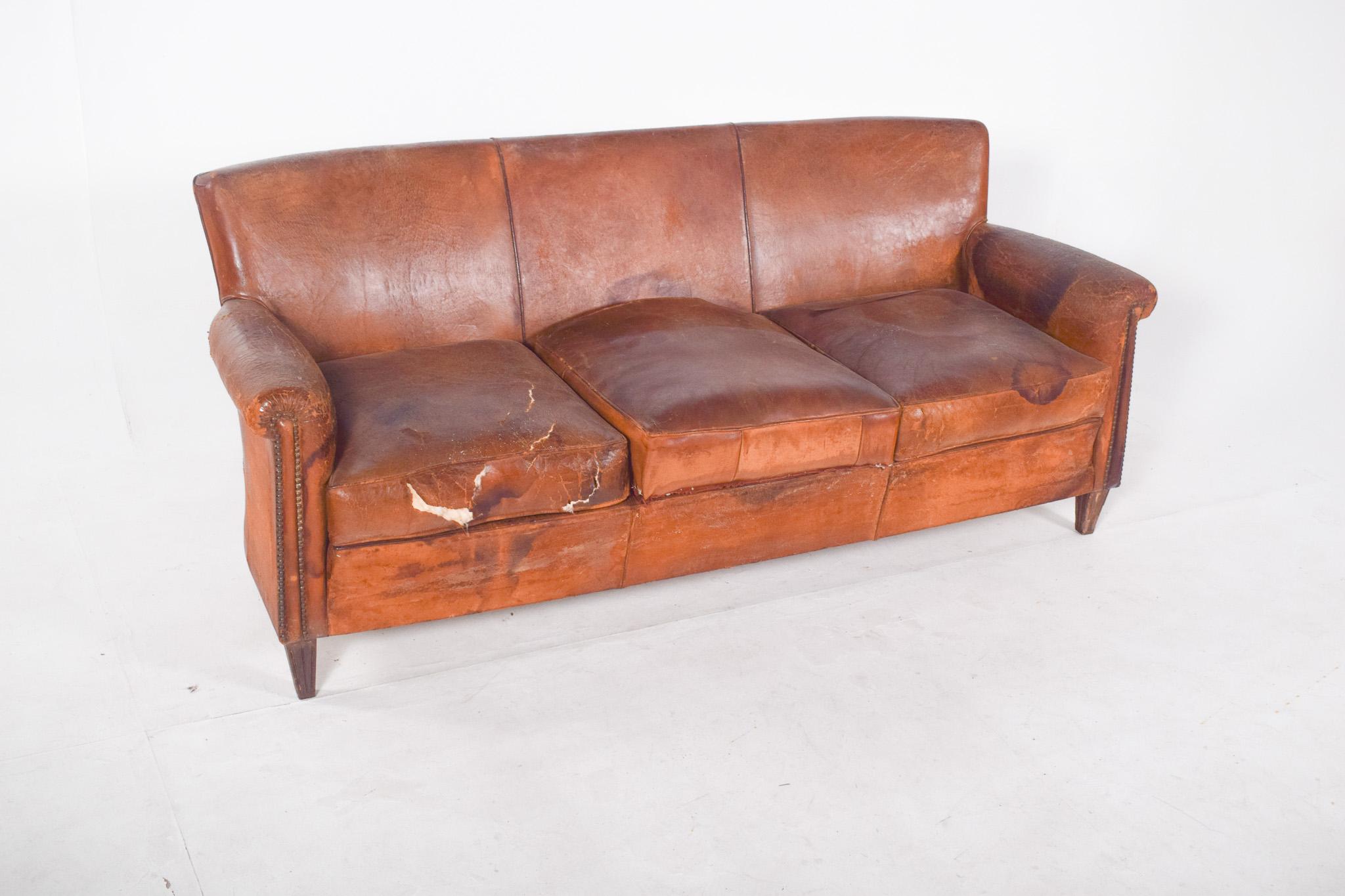 Three-seater sofa, brown leather. The leather shows clear signs of wear, with visible tears, stains and dry areas, particularly on the left-hand seat and armrests. The cushions are loose and show signs of use, with loss of volume and pronounced