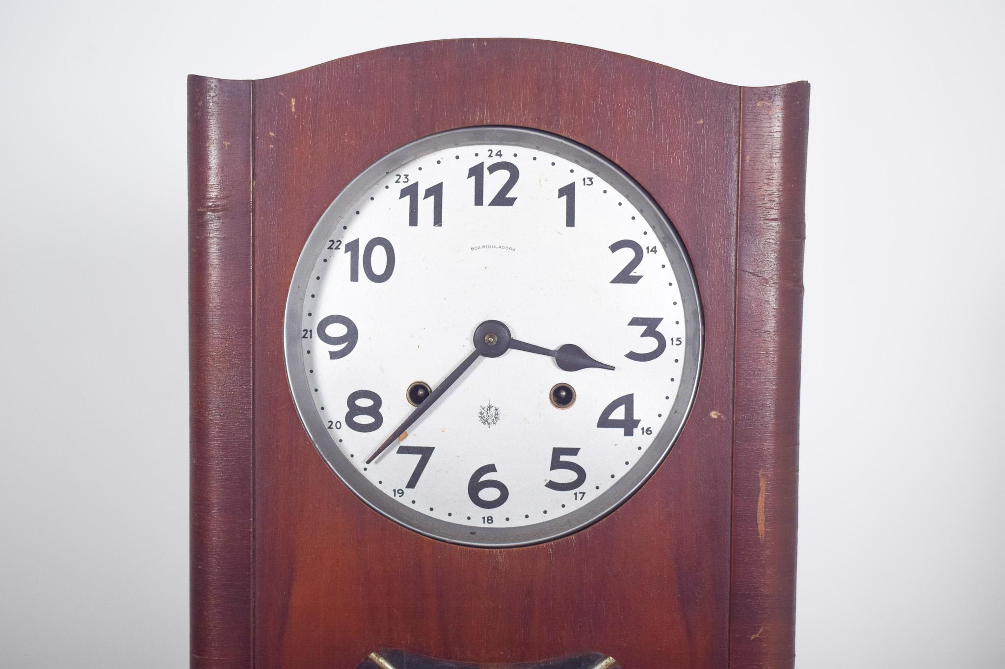 Portuguese wall clock, Art Deco.  With straight lines and gentle curves, the frame is made of varnished wood, with a rectangular shape and slightly arched top. The dial is white with black Arabic numerals and an internal 24-hour marker. The metal