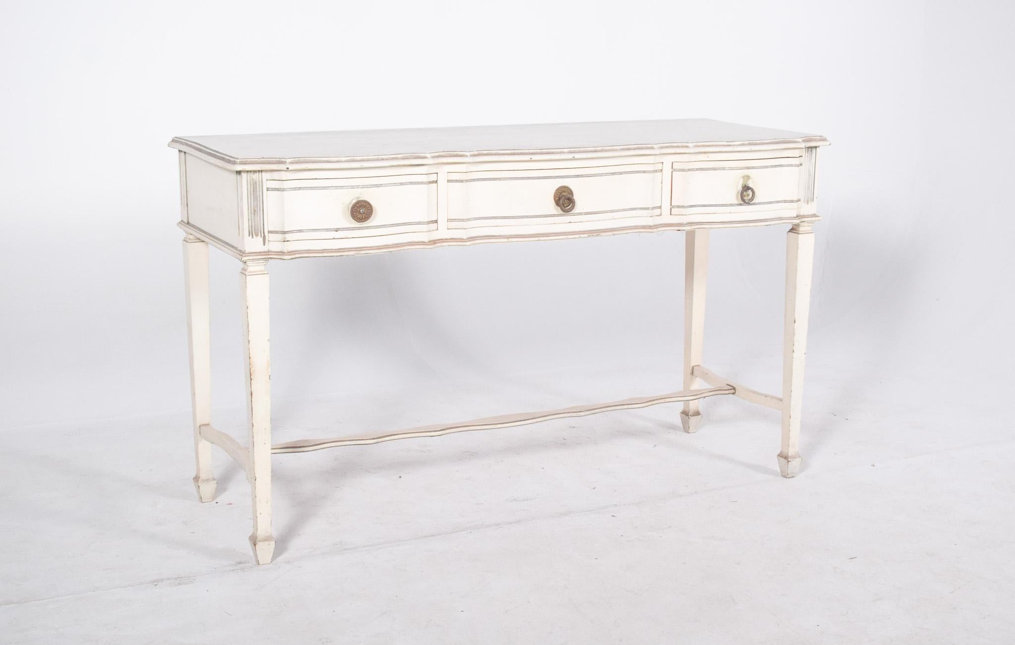 White painted console. The wooden structure has elegant lines with a slight undulation on the front, where three proportionally sized drawers stand out, decorated with classic-style circular metal handles. The tall, straight legs end in cut-out feet