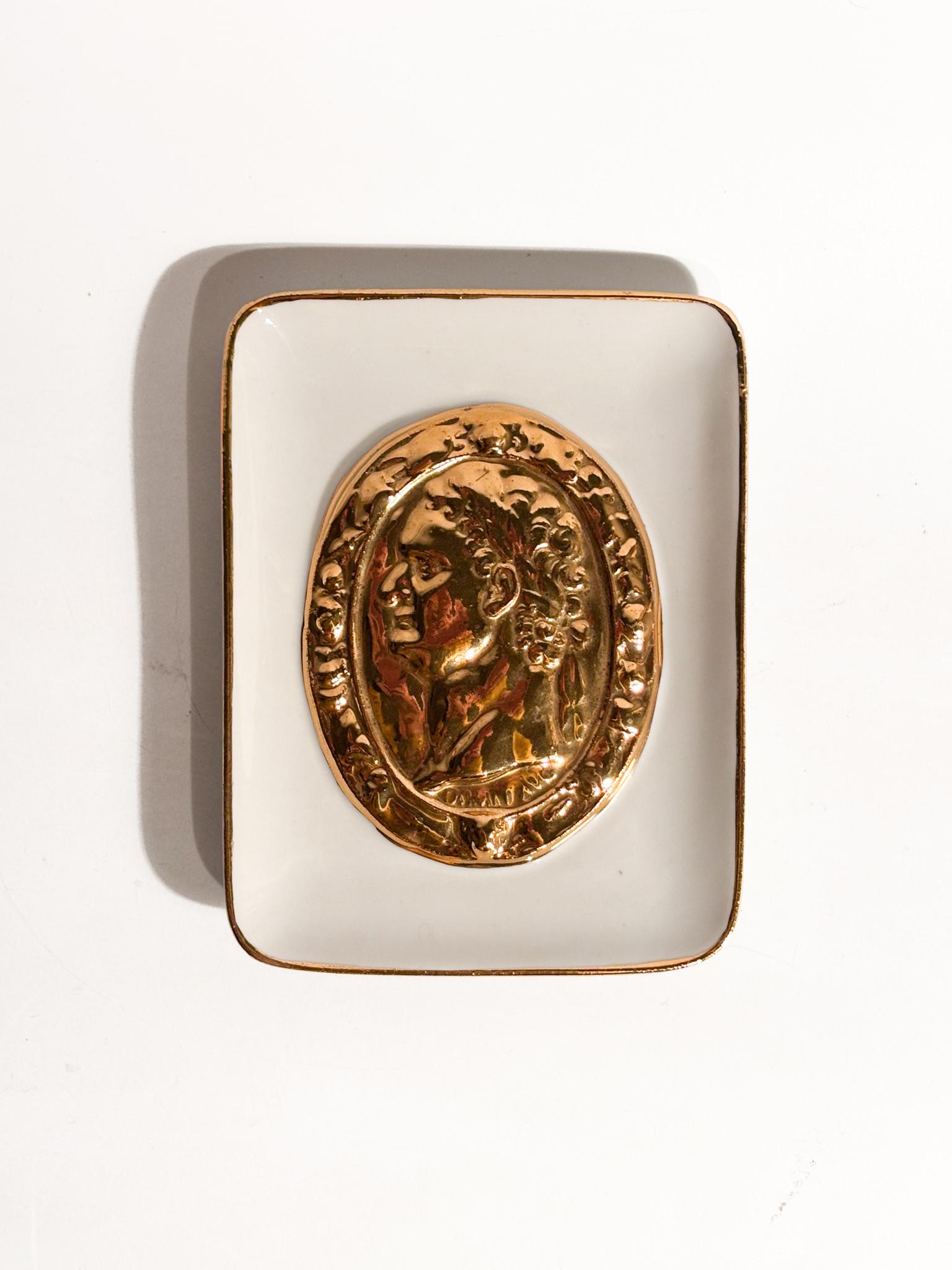 Penderie à vaschetta avec décor à la Moneta Romana, réalisée par Piero Fornasetti dans les années 50

Ø cm 11 h cm 14

Posacenere a vaschetta in ceramica smaltata a fondo bianco centrato, con decoro dorato ritraente una moneta romana a rilevo con