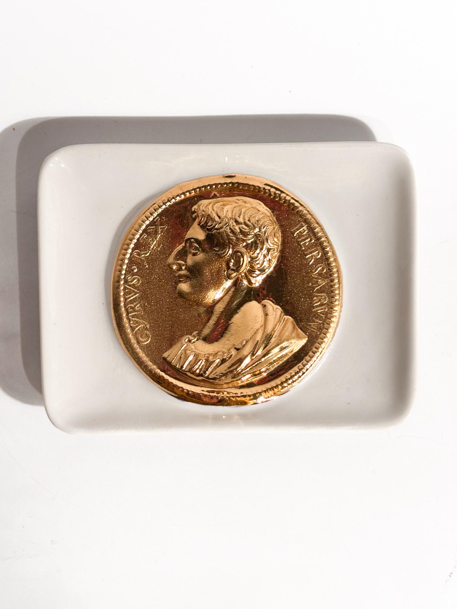 Posacenere a vaschetta con decoro a Moneta Romana, realizzato da Piero Fornasetti negli anni '50

Ø cm 11 h cm 14

Posacenere a vaschetta in ceramica smaltata a fondo bianco centrato, con decoro dorato ritraente una moneta romana a rilevo con volto