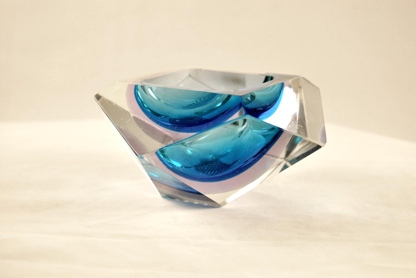 Splendido posacenere svuotatasche in vetro sommerso di Murano, anni '70
The 'pentagon-shaped object, is finely crafted with various facets that create beautiful color reflections between blue and seawater. Perfect condition, like new.
SUBMERGED. It