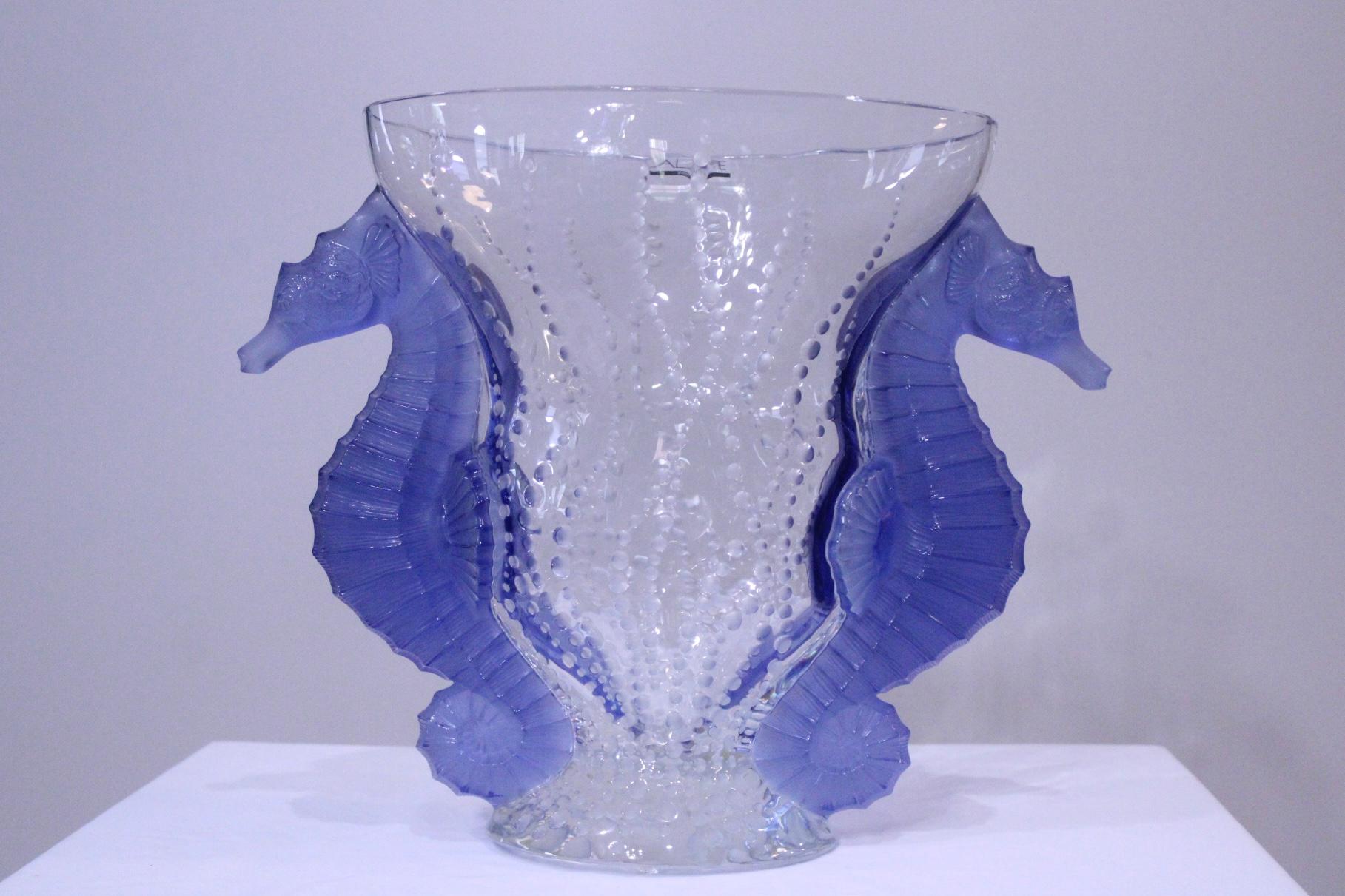 Un sorprendente vaso in vetro in edizione limitata, decorato con bolle in aumento e con due cavallucci marini lilla come manici. Presenta colori favolosi e dettagli finissimi rifiniti a mano, firmati Lalique France e numerati 3/99. Dalla rarissima