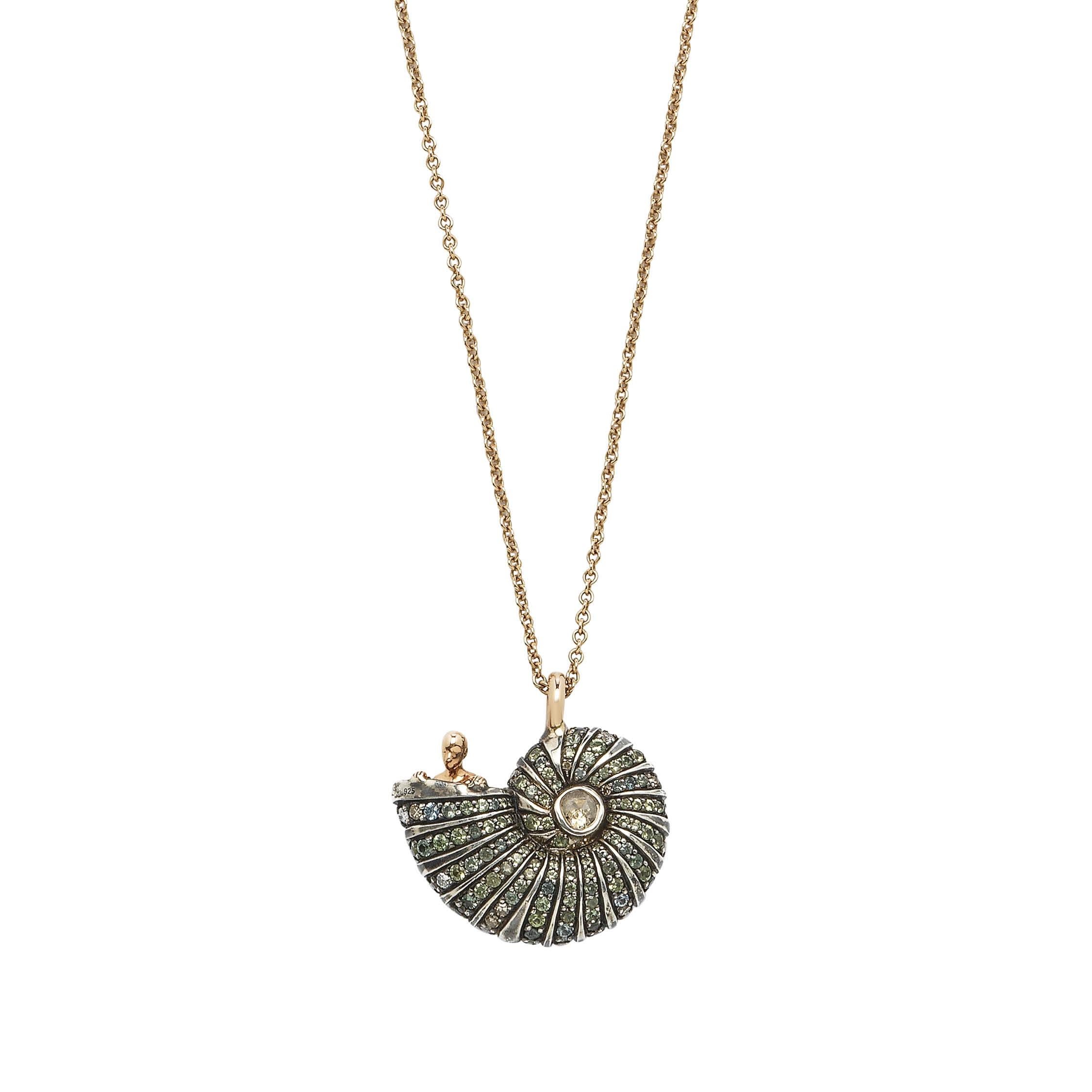This pendant necklace is fashioned in 18k rose gold and sterling silver as a pretty shell, out of which emerges an 18k rose gold human figure, inspired by Hieronymus Bosch’s fantastical paintings. The shell is embellished with blue and green