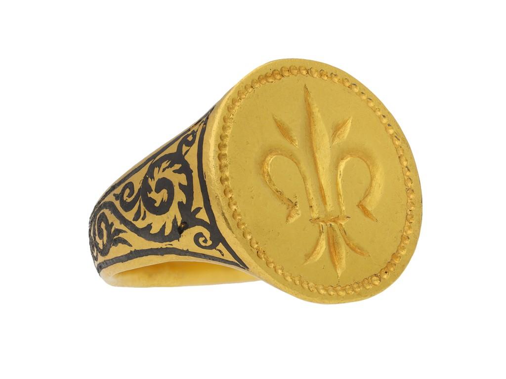 Post Medieval gold fleur-de-lis signet ring. A heavy yellow gold signet ring, the central circular plaque engraved with a prominent fleur-de-lis motif and framed by incised beaded edging, the integrated trumpeting shoulders feature scrolling