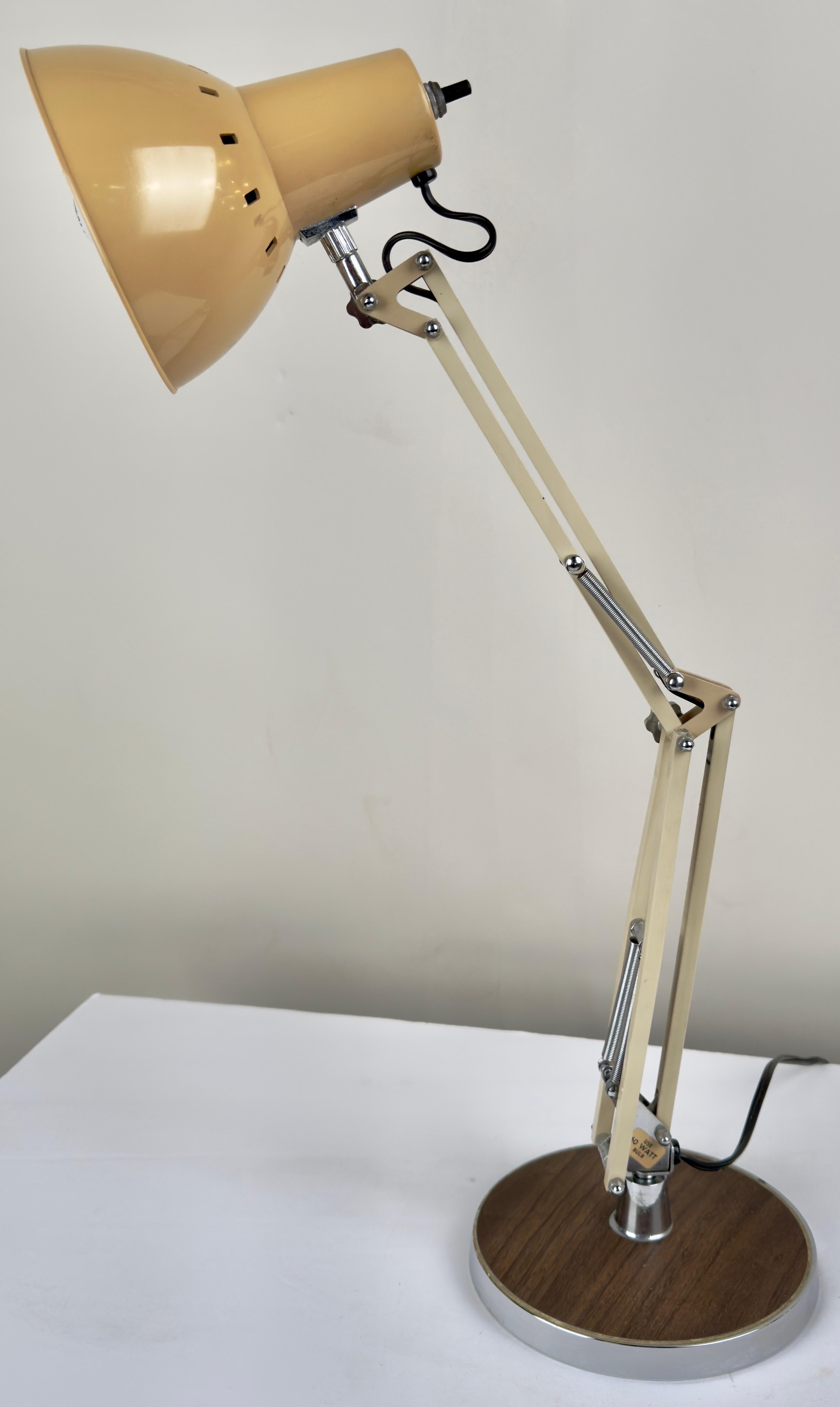 A Post Modern Articulating Architects Drafting Lamp in Tan, crafted by Electrix, Inc. Standing atop a round base adorned in a warm wood finish, this lamp boasts a sturdy metal construction delicately coated in a soothing tan hue. Its articulating