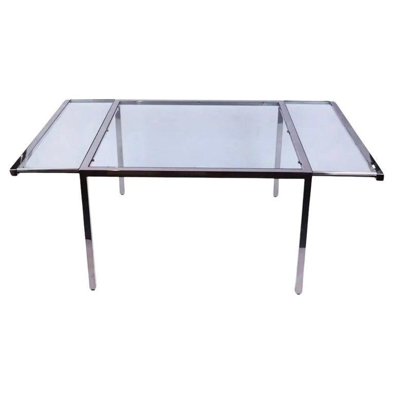 Table de salle à manger post-moderne en verre et chrome circa 1970 avec support coulissant pour les feuilles de verre. Cadre en tube chromé avec plateau carré en verre épais et 2 vantaux en verre épais. La table est équipée d'une rallonge sur les