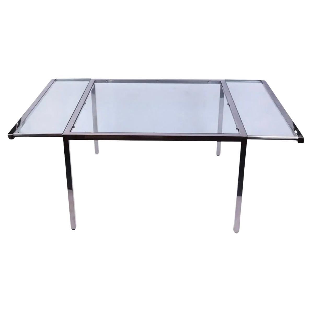 Post modern glass and chrome dining table circa 1970 with pullout support for glass leaves. Chrome Tube frame with thick glass square top and 2 thick glass leaves. Has an extension on the left and right side of the table that pull out. Leaves drop