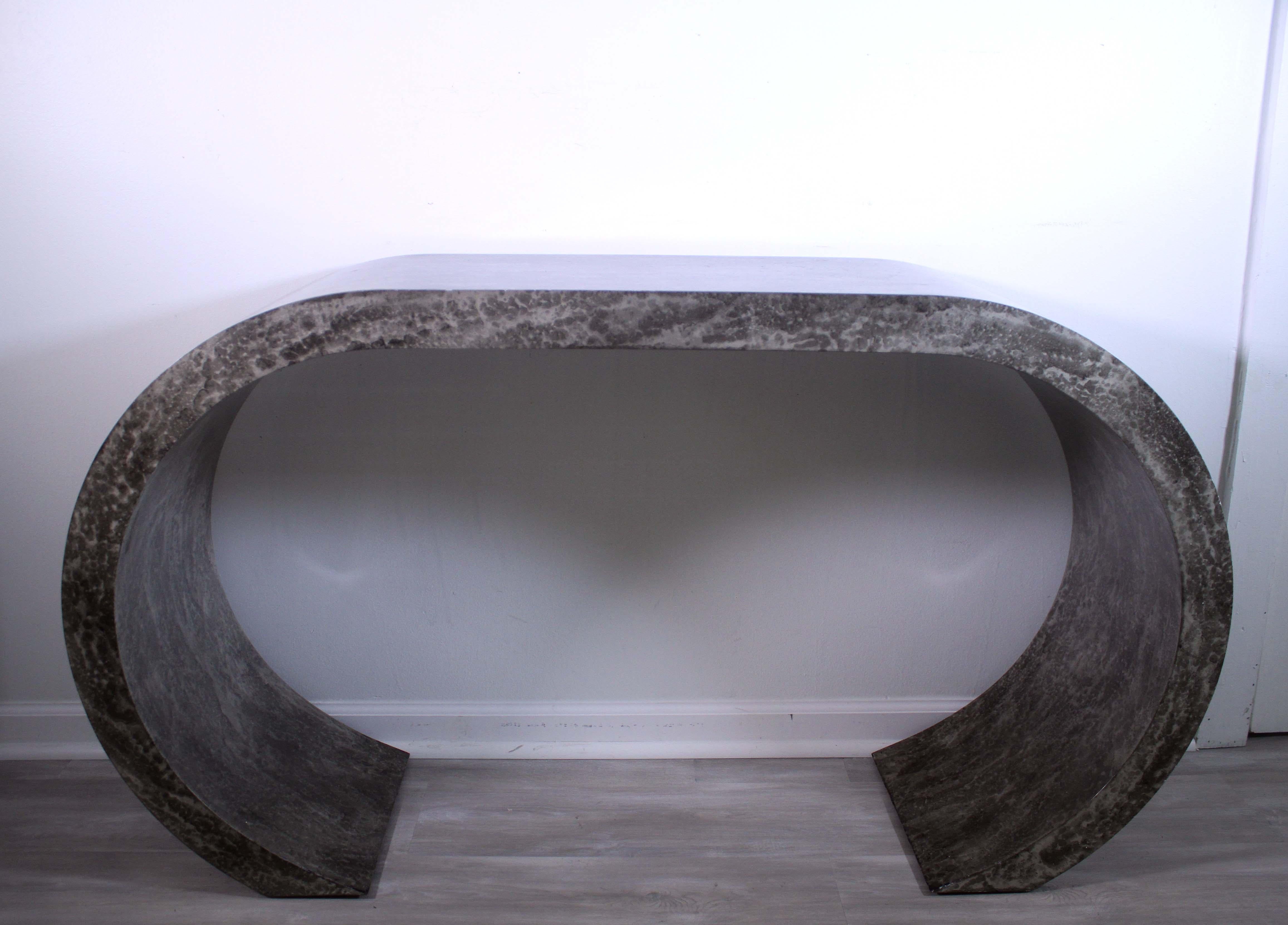 This postmodern curved faux stone console table is a contemporary and unique piece of furniture perfect for adding a modern touch to any space. The sleek design features a curved profile and an eye-catching faux stone top. The sturdy metal frame