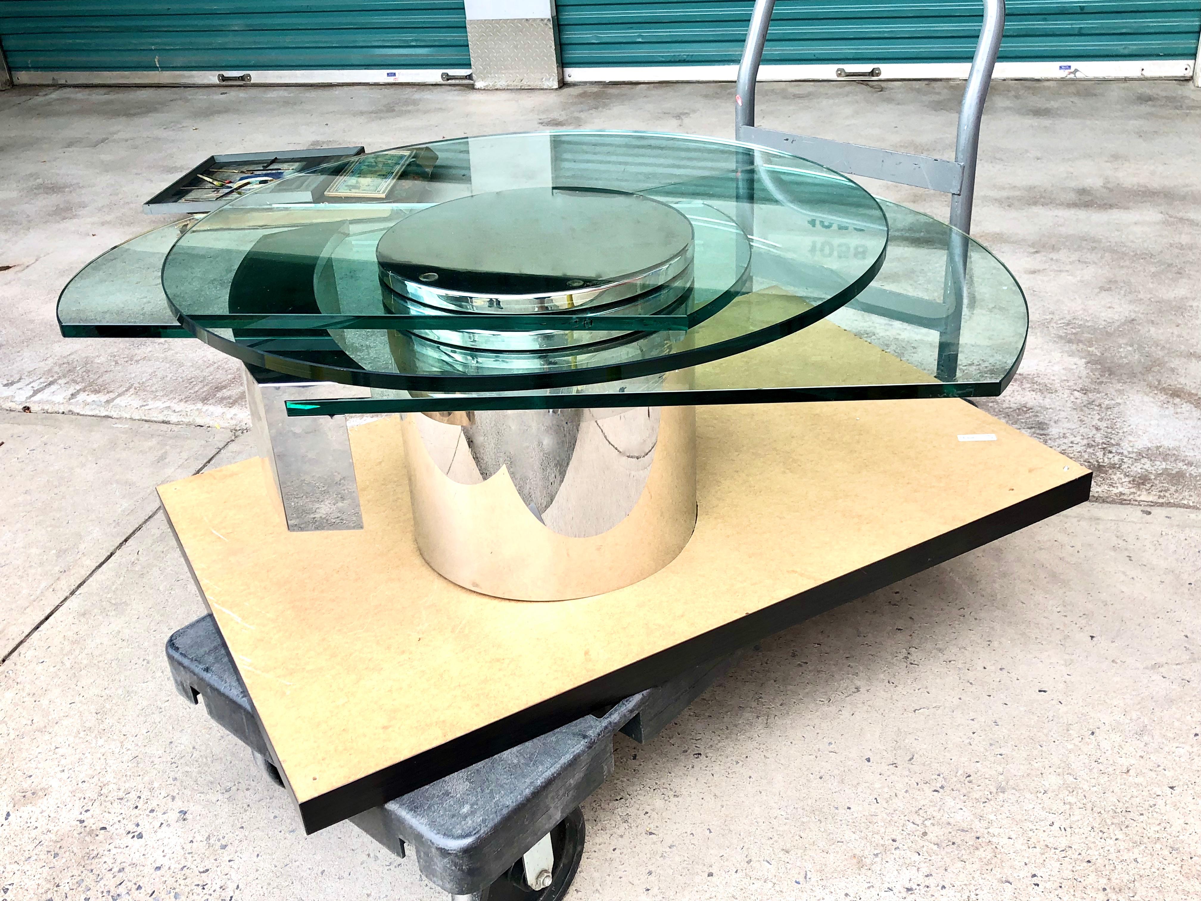 Iconic postmodern design by Dakota Jackson. The steel base features three levels of thick glass. Referencing the self-winding clock, the two “hands” of the table shift under and around the round top like the hands of the clock that hover ever so