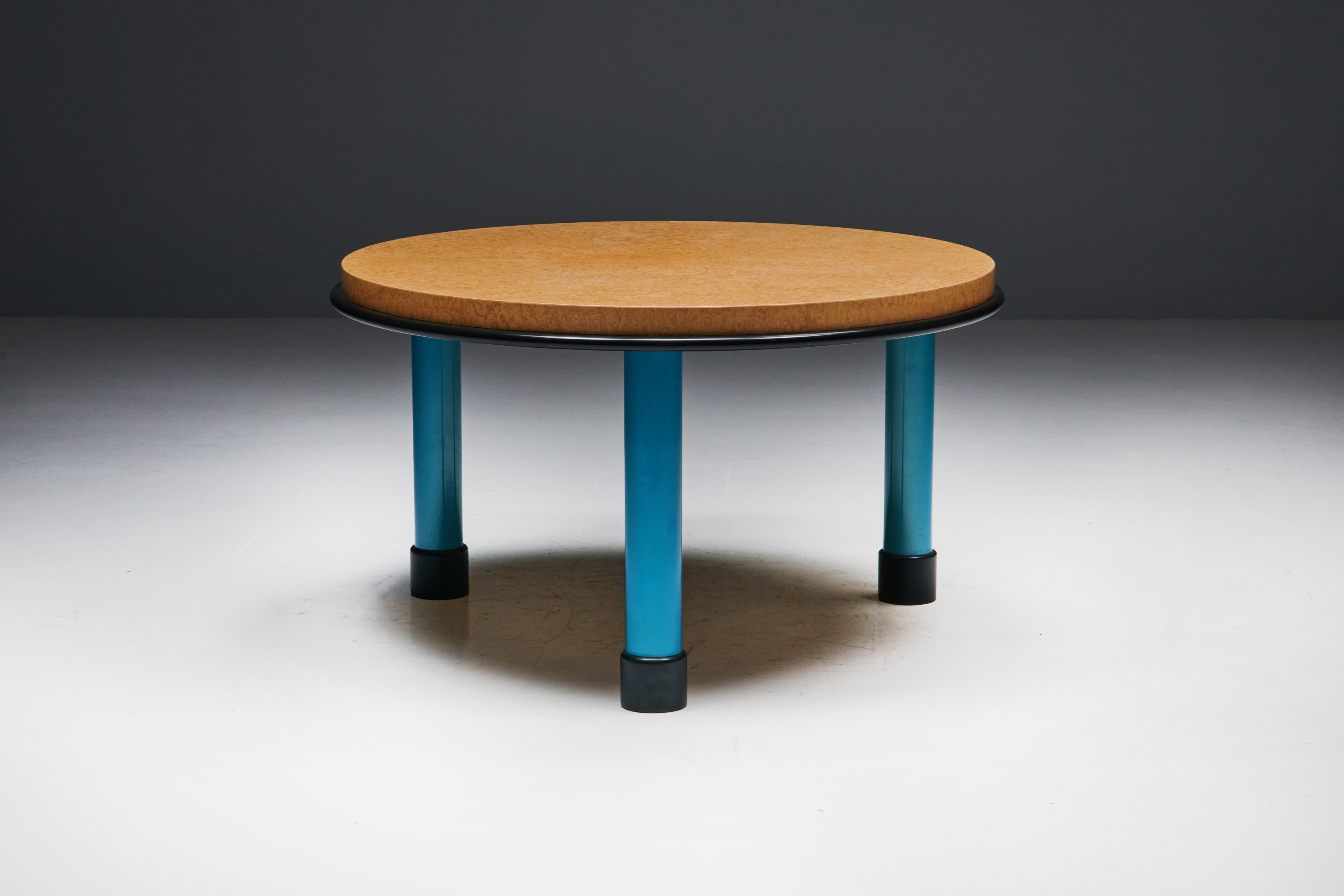 Round Memphis table featuring a luxurious burl wood top paired with elegantly crafted legs in a vibrant blue lacquer, paying homage to the distinctive design philosophy of Ettore Sottsass. Sottsass was a prominent Italian architect and designer of