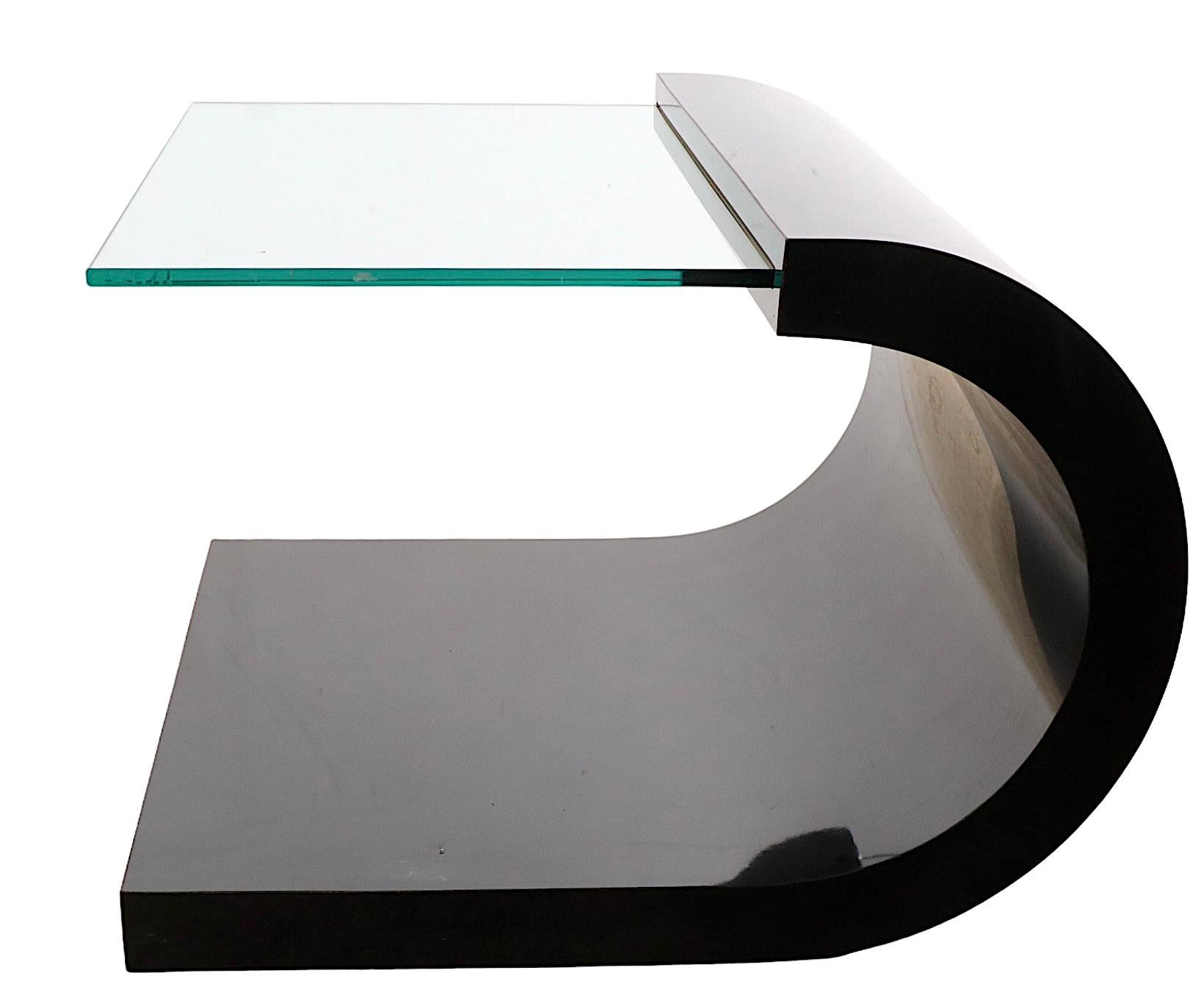 Chic  Post Modern architectural side, or end, table in shiny black formica with a thick plate glass shelf. The curved black base supports the cantilevered glass shelf, creating a dramatic and bold profile, as shown. This example is in very good,