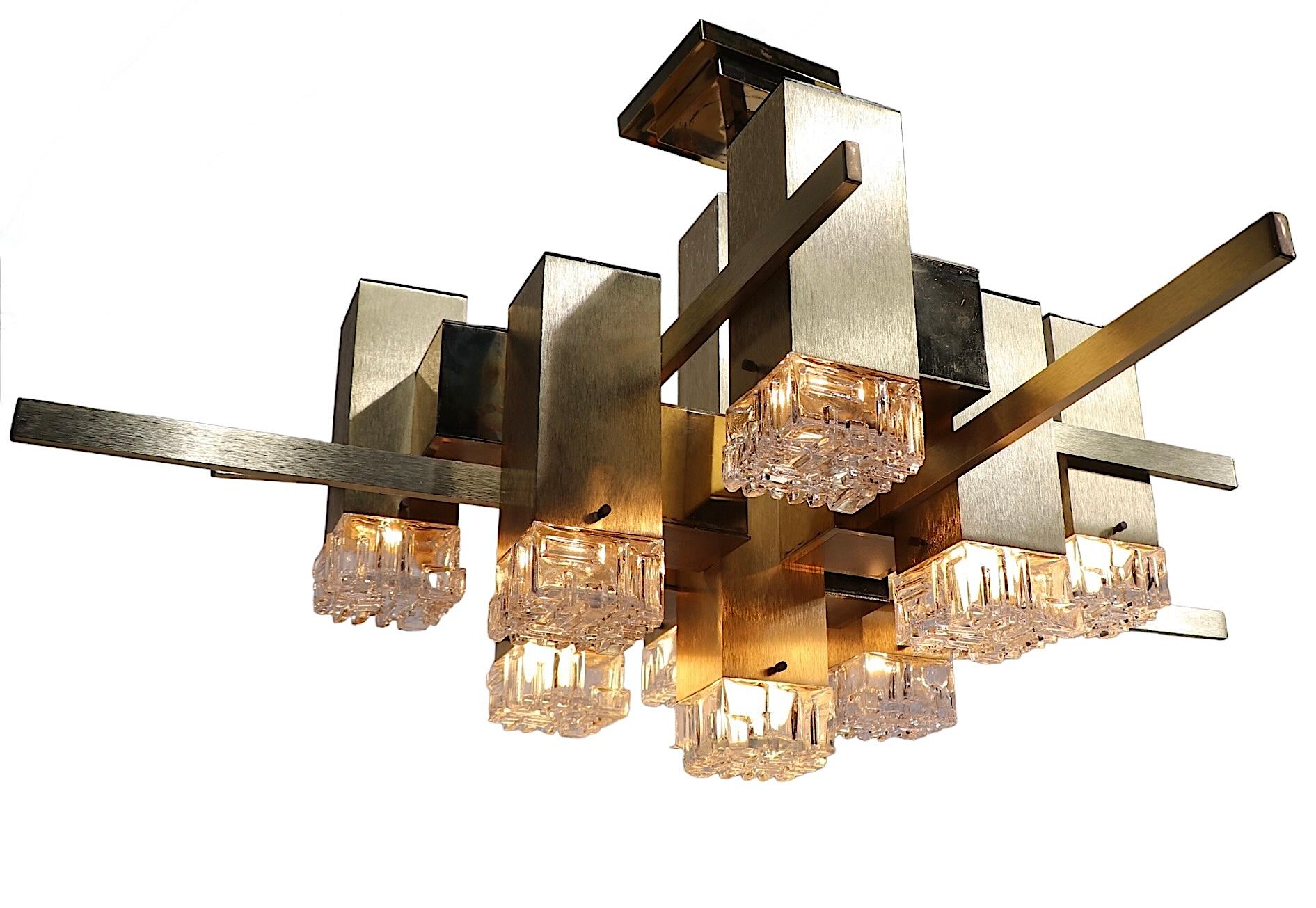 Chic Post Modern nine light chandelier, designed by Gaetano Sciolari for Sciolari Lighting. The fixture features nine rectangular lights each with a brass colored metal box which terminates in the cubic clear glass shade. The chandelier is in good,