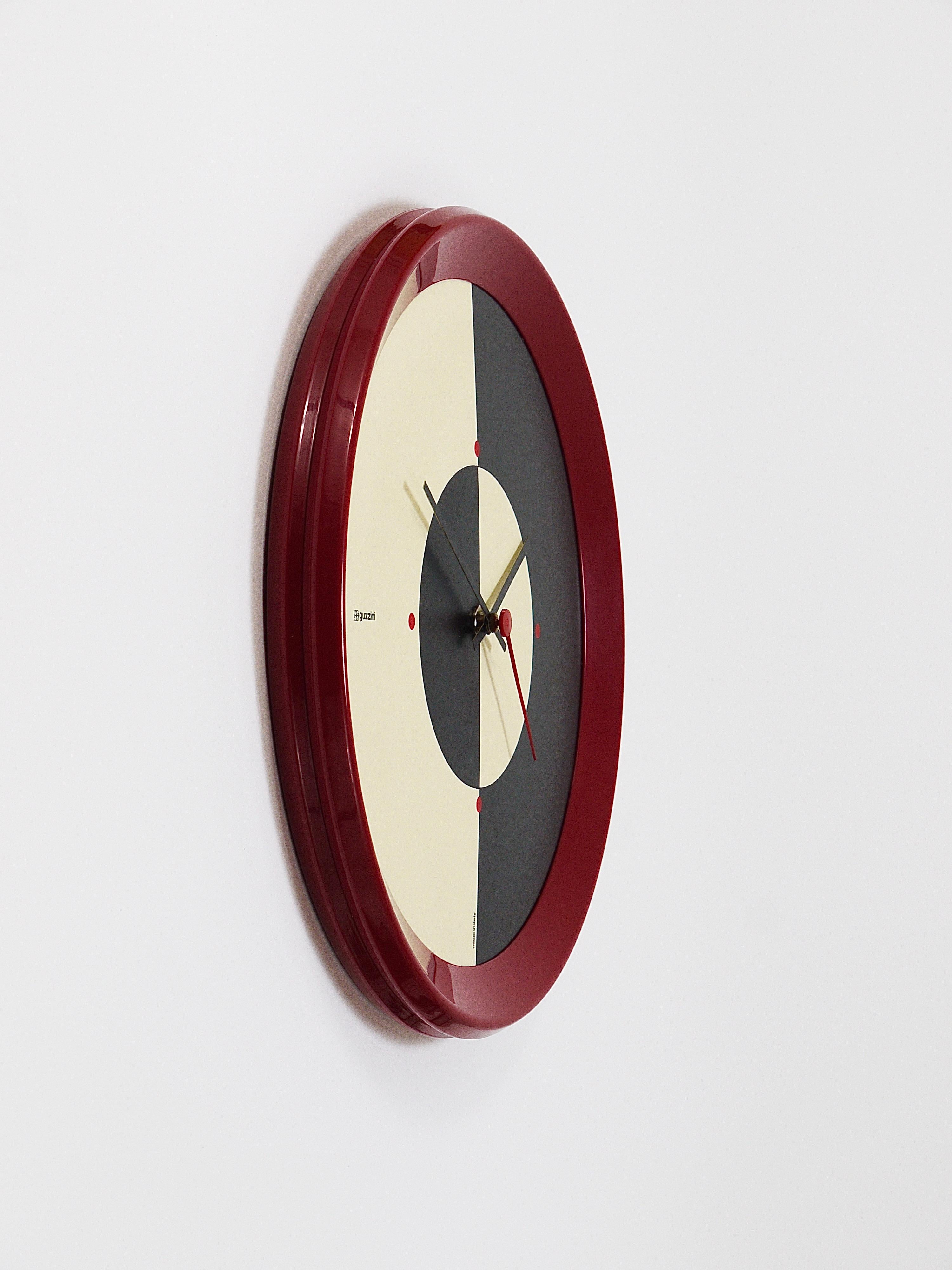 A beautiful postmodern Memphis-style wall clock from the 1980s. Designed by Bruno Gecchelin, executed by Guzzini, Italy. The housing is made of bordeaux dark red plastic, the black and white clocks face shows wonderful geometric graphics and has red