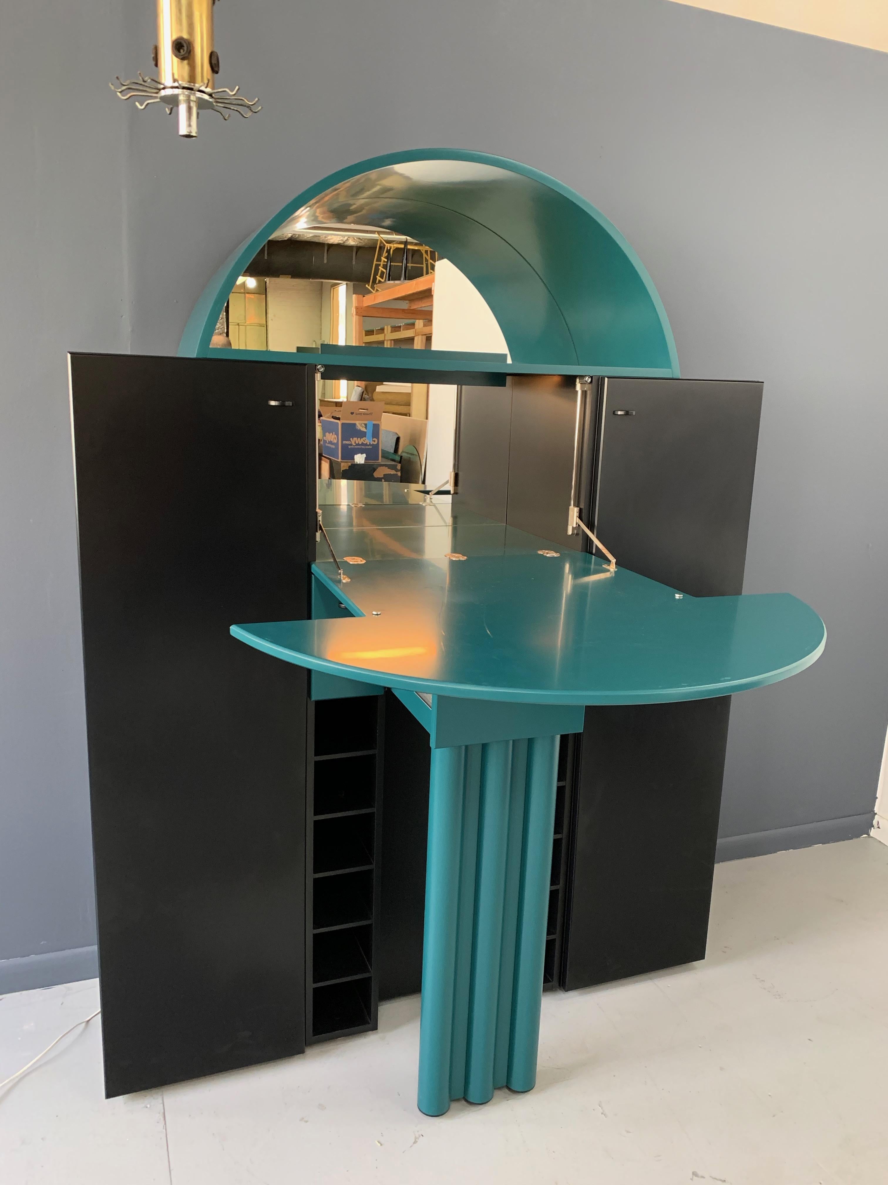 Postmodern bar from German Manufacturer Interlübke, produced in the 1970s.

Arched center door folds down to reveal a lighted mirrored space to hold bottles and glasses. There are also many drawers and spaces to keep bar accoutrement.