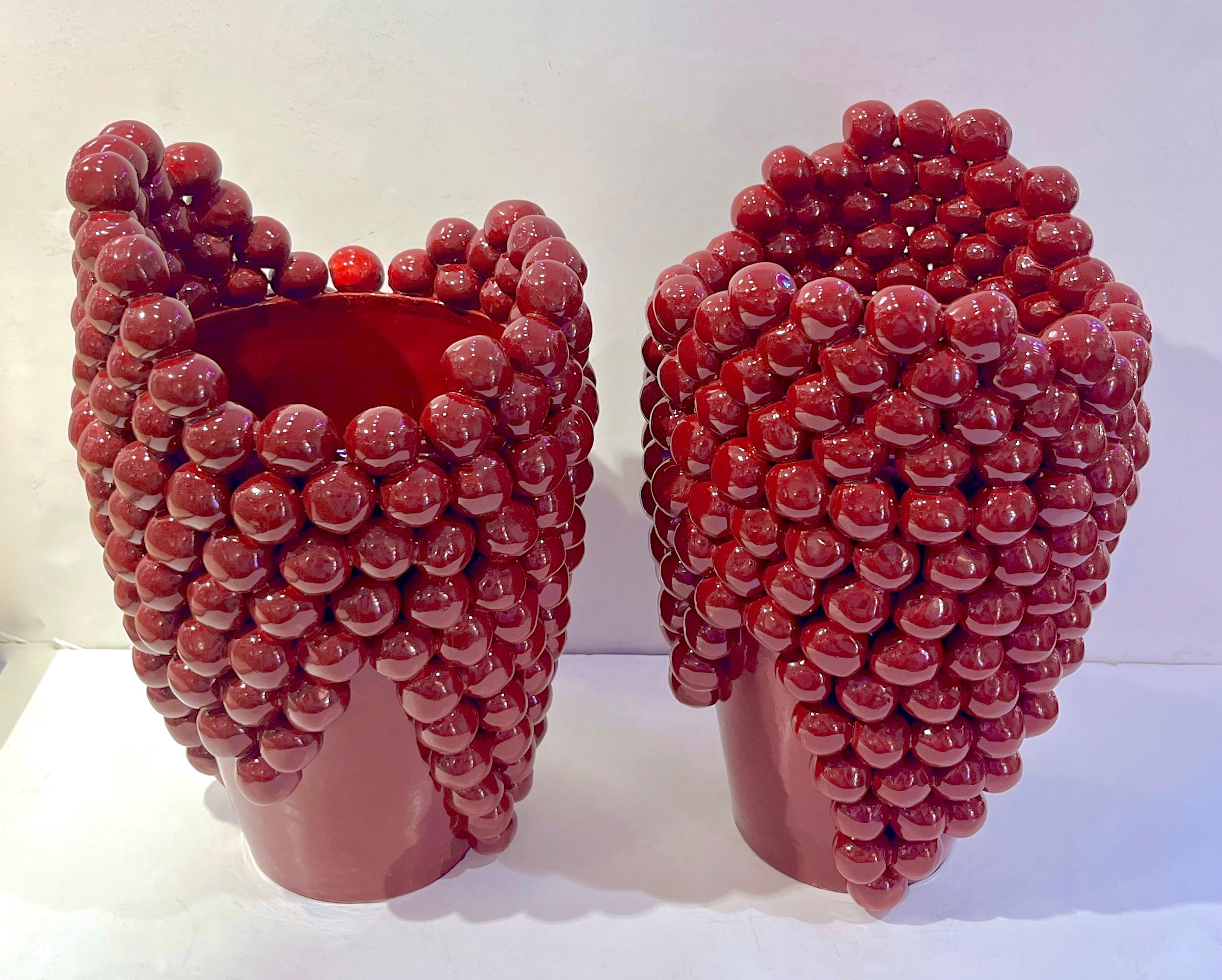 This early 21st-century Northern Italian ceramic pair of organic sculptural vases, entirely handcrafted in Italy, presents an unusual post-modern style, the asymmetrical shape makes them resemble urns with overflowing grape clusters. Their color