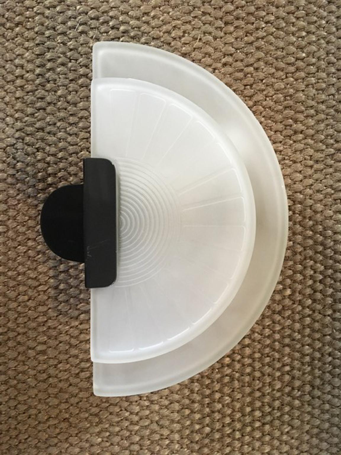 This is an engaging wall light in satin glass that has the base in aluminum lacquered in polished black color. The two satin sheet glass are put as lampshades. They have an harmonious half moon shape and they are engraved with geometrical drawings.