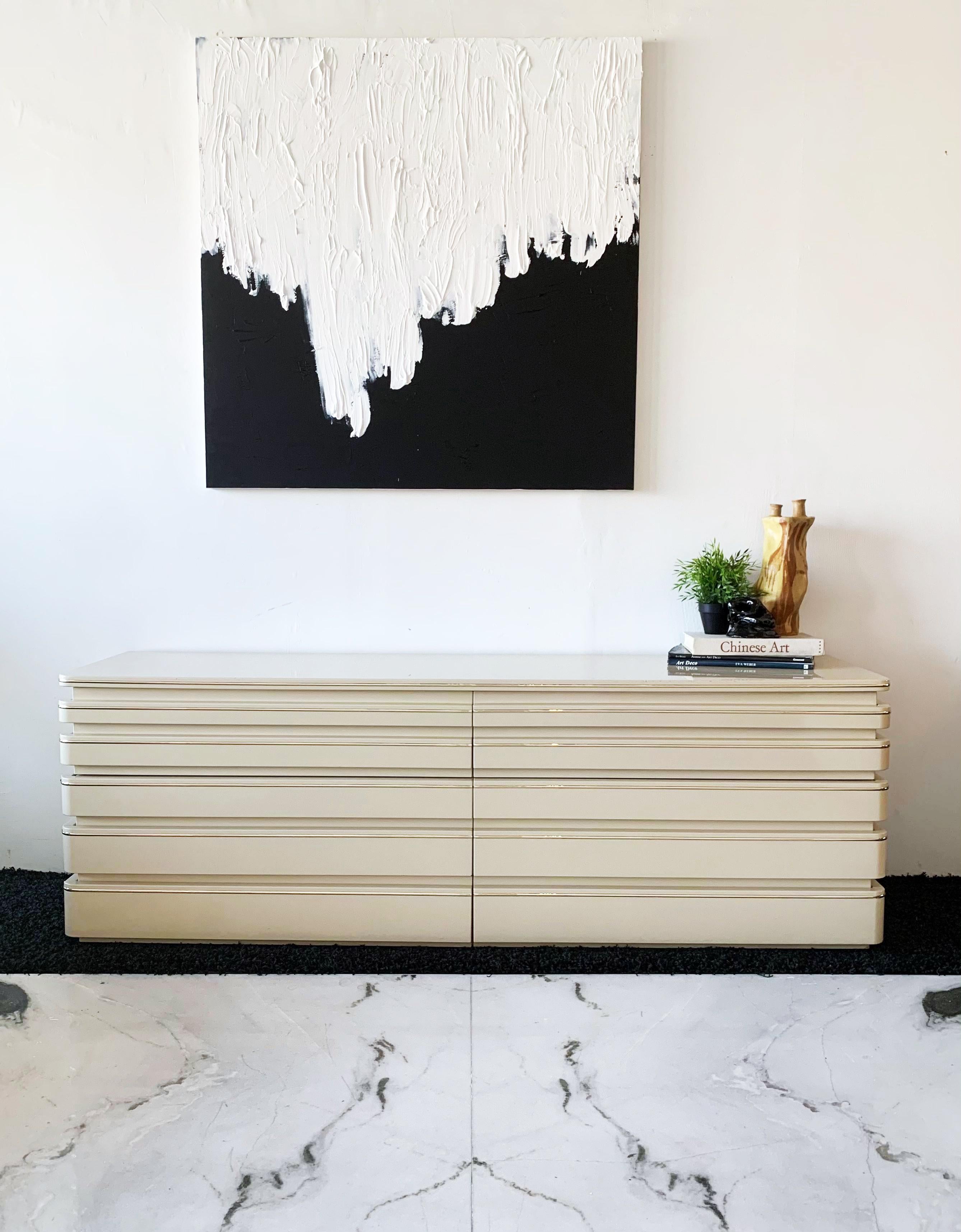 Available right now I have this stunning post modern cream lacquered sideboard or dresser by Roger Rougier. This Rougier sideboard features brass piping / detailing as well as a brass plinth / platform along the bottom of the piece.

This piece